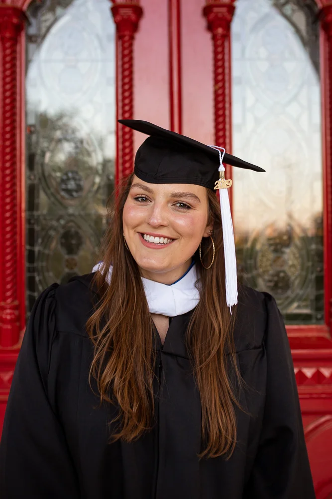 Female college senior standing in front of Red Doors of St. Edward’s University. Photo by Erin Reas Austin, TX senior photographer.