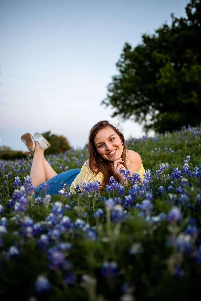 St. Edward’s University college graduate sitting in field of bluebonnets wearing yellow check blouse. Photo by Erin Reas senior photographer in Austin, TX