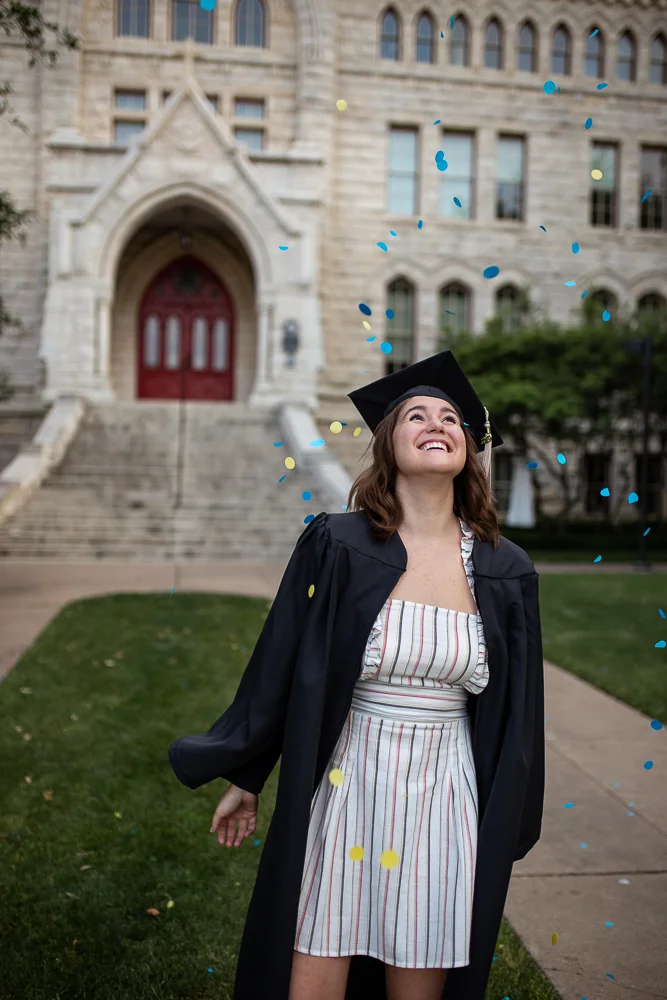 Female college graduate throwing blue and yellow confetti in the air while looking up. Photo by Erin Reas senior photographer in Austin, TX