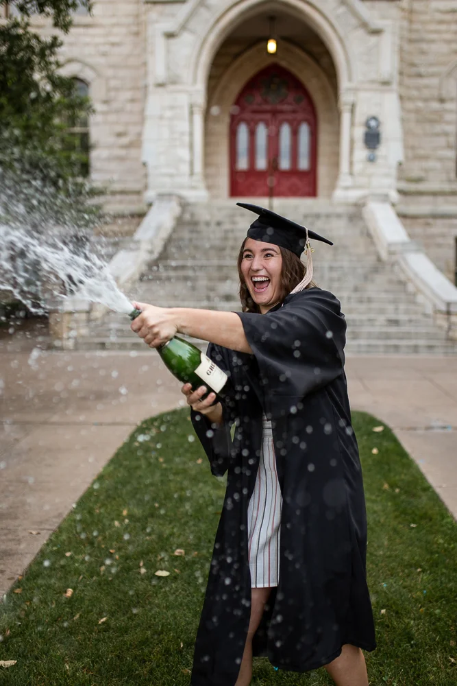 College senior popping bottle of champagne and spraying it at St. Edward’s University. Photo by Erin Reas senior photographer in Austin, TX.