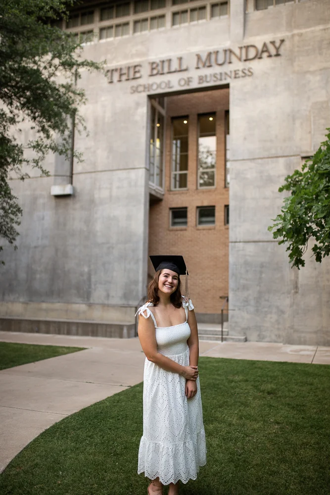 Female college graduate wearing white dress standing in front of Trustee Hall at St. Edward’s University. Photo by Erin Reas senior photographer in Austin, TX