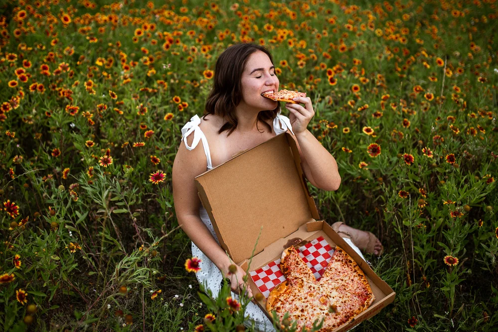 College graduate at St. Edward’s University eating pizza in a field of Indian Paintbrushes. Photo by Erin Reas senior photographer in Austin, TX. Pizza from Southside Flying Pizza