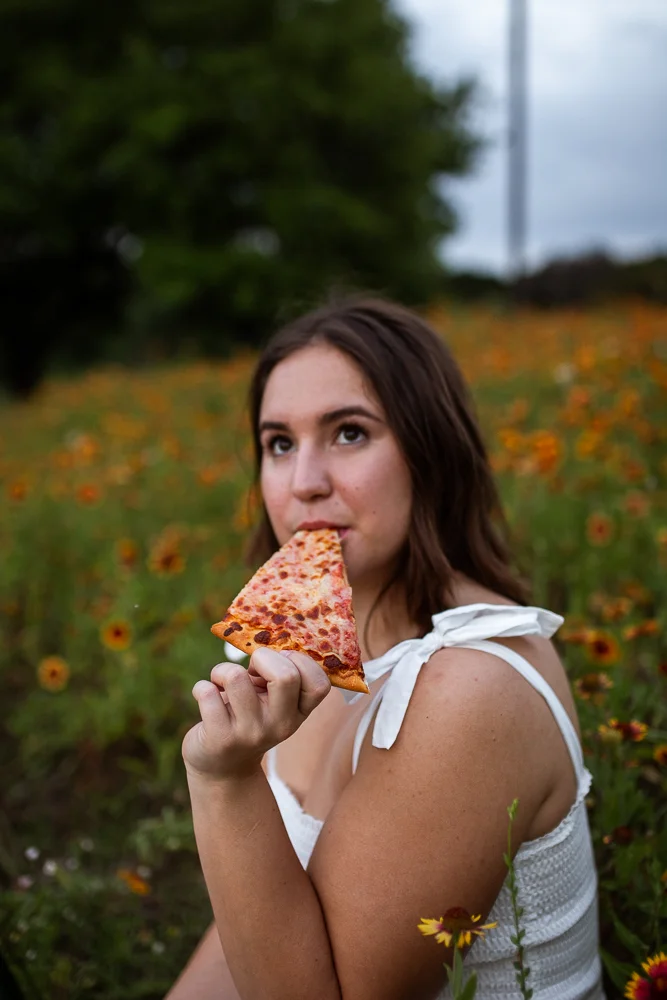 College graduate at St. Edward’s University eating pizza in a field of Indian Paintbrushes. Photo by Erin Reas senior photographer in Austin, TX. Pizza from Southside Flying Pizza