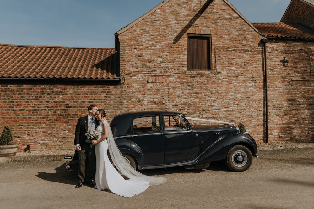 Bride and groom next to their wedding car outside The Normans wedding venue. Photo by Louise Anna Photography.jpg