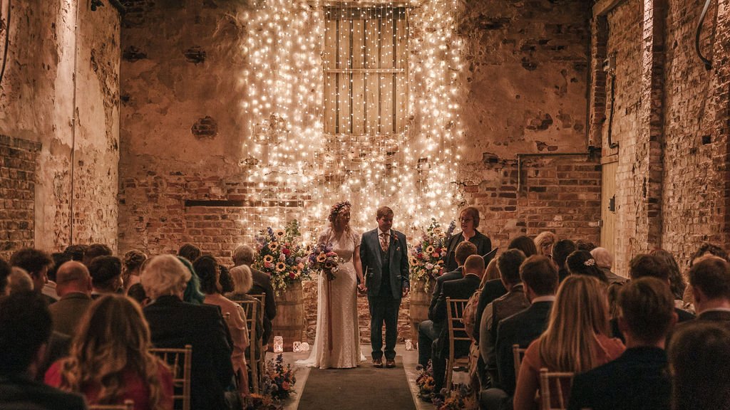 22_Bride and groom and the fairy lights in The Normans wedding venue Ceremony Barn. Photo by Jules Barron.jpg