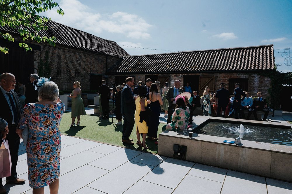 05_Wedding guests enjoy the sunshine in The Normans Courtyard. Photo by Charlotte White (2).jpg