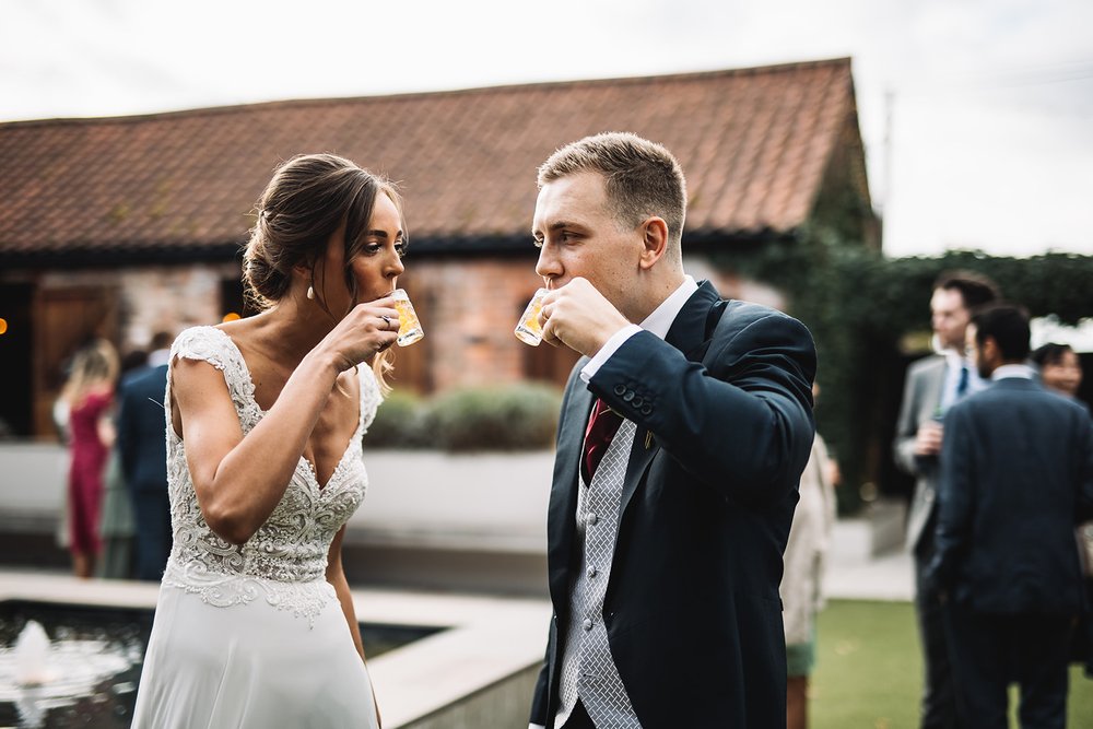 21_Bride and groom drink mini pints in The Normans wedding venue Courtyard. Photo by Lumiere Photographic.jpg