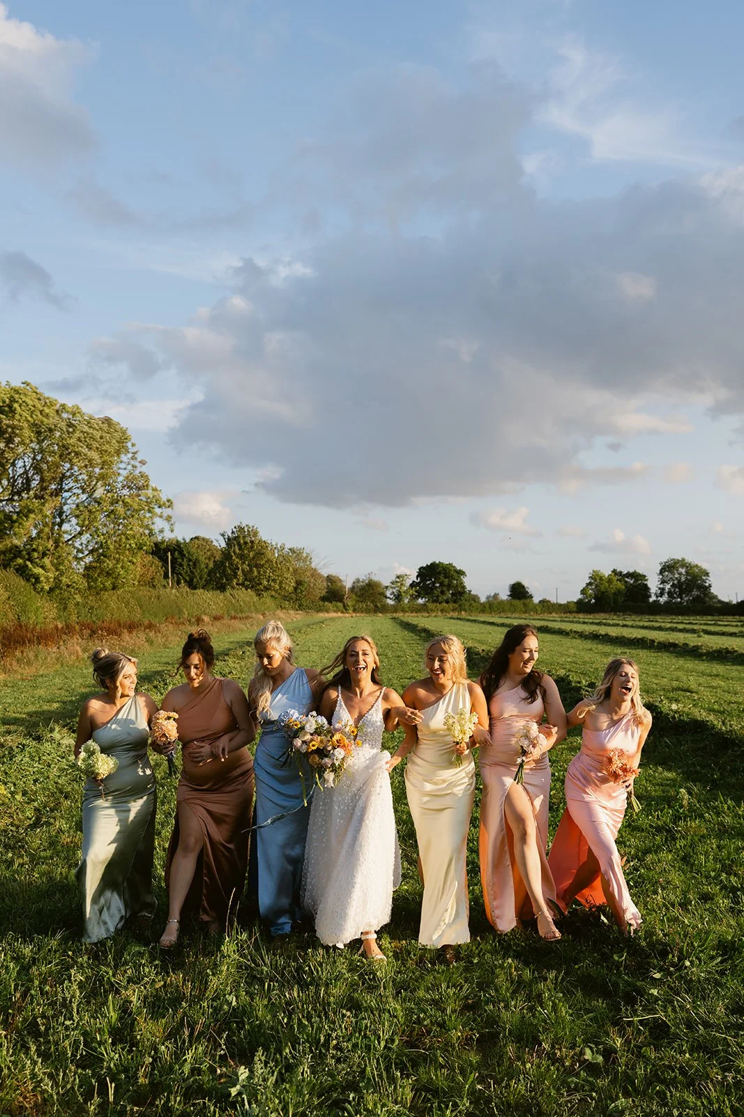 bride-bridesmaids-walking-meadow-sunset.jpg