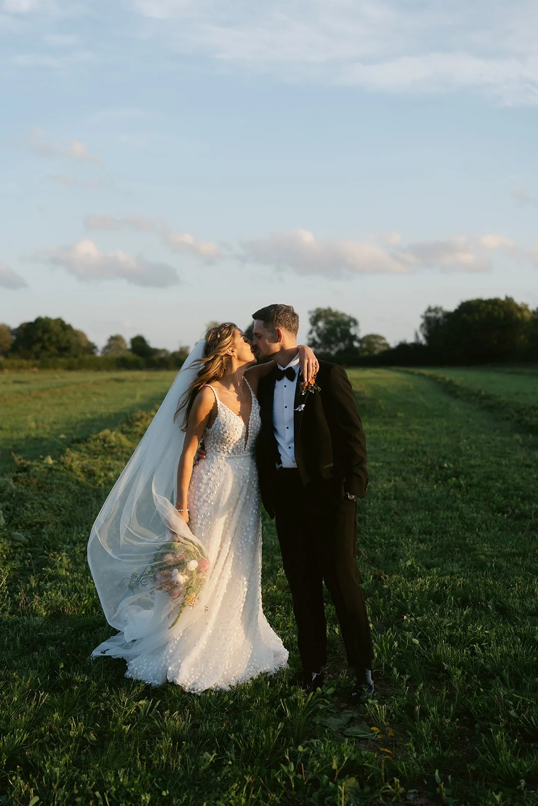 newlyweds-kissing-sunset-field-flowing-veil.jpg