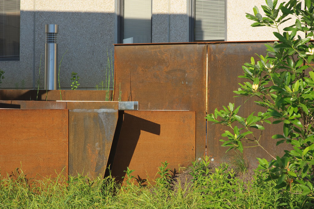 A custom-detailed scupper conveys plaza stormwater beyond the new weathering steel alloy walls and into a biofilter planted with Sweetbay Magnolia and other native Virginia plants.