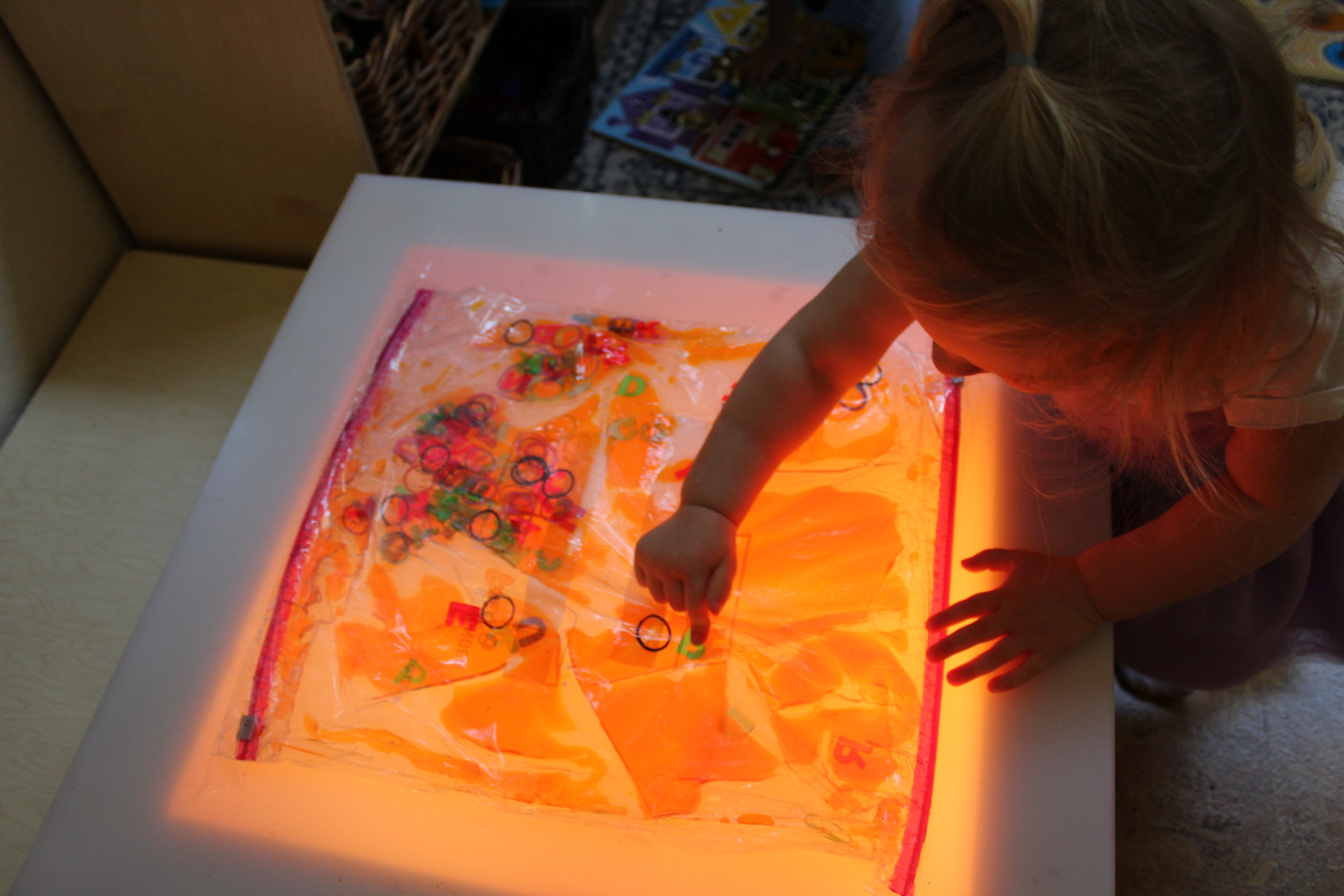  Sensory bags are inviting to toddlers.&nbsp; Sensory invitations to play is a delightful resource that encourages children to explore their sense of touch and sight.&nbsp;&nbsp;Madeline appears intrigued as she explores the sensory bag on the lighta