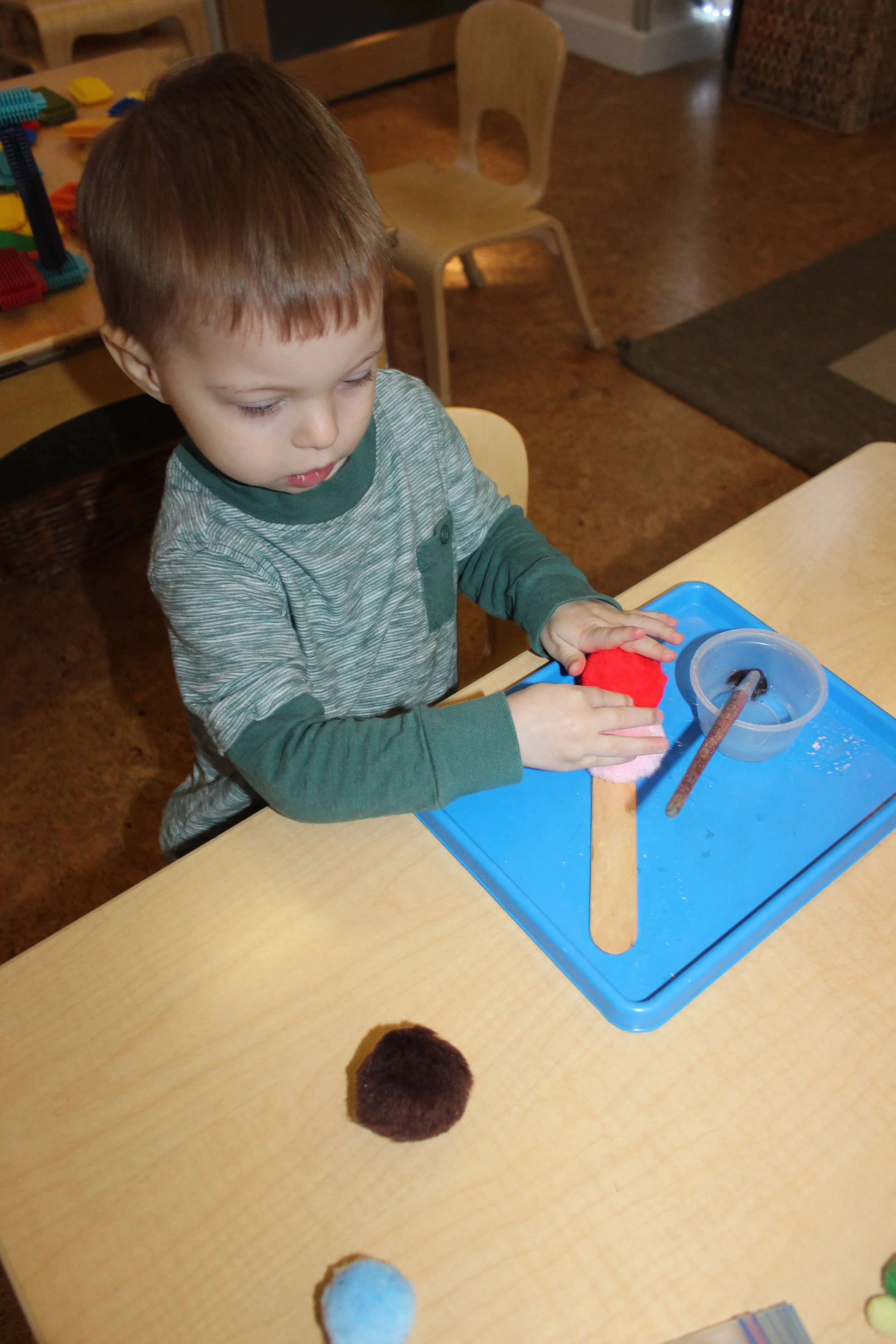  The children were gluing and pasting their choice of color pom poms on the Popsicle stick, creating caterpillars. They used small and big Popsicle sticks, and paint sticks. These caterpillars will be displayed in the classroom wall.   