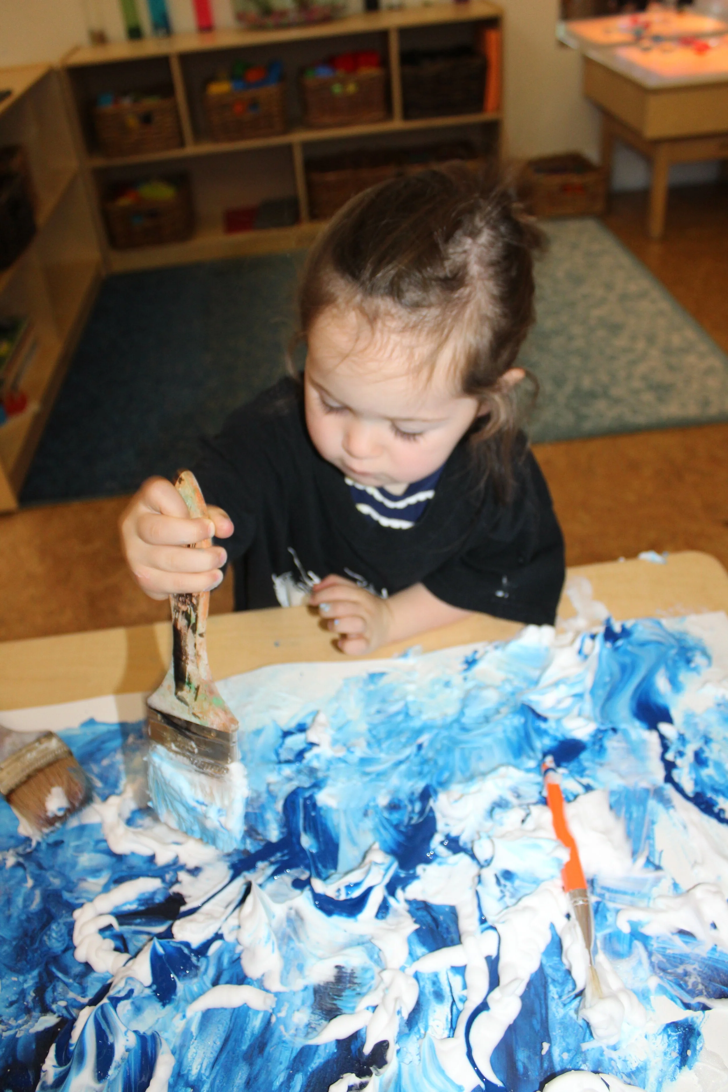  As Annabelle lightly pressed with the paintbrush, she noticed blue and white colors and dark and light shades of blue. She dabbed with the paintbrush and articulated, "What is that?" Annabelle appeared curious as she mixed the materials and made sho