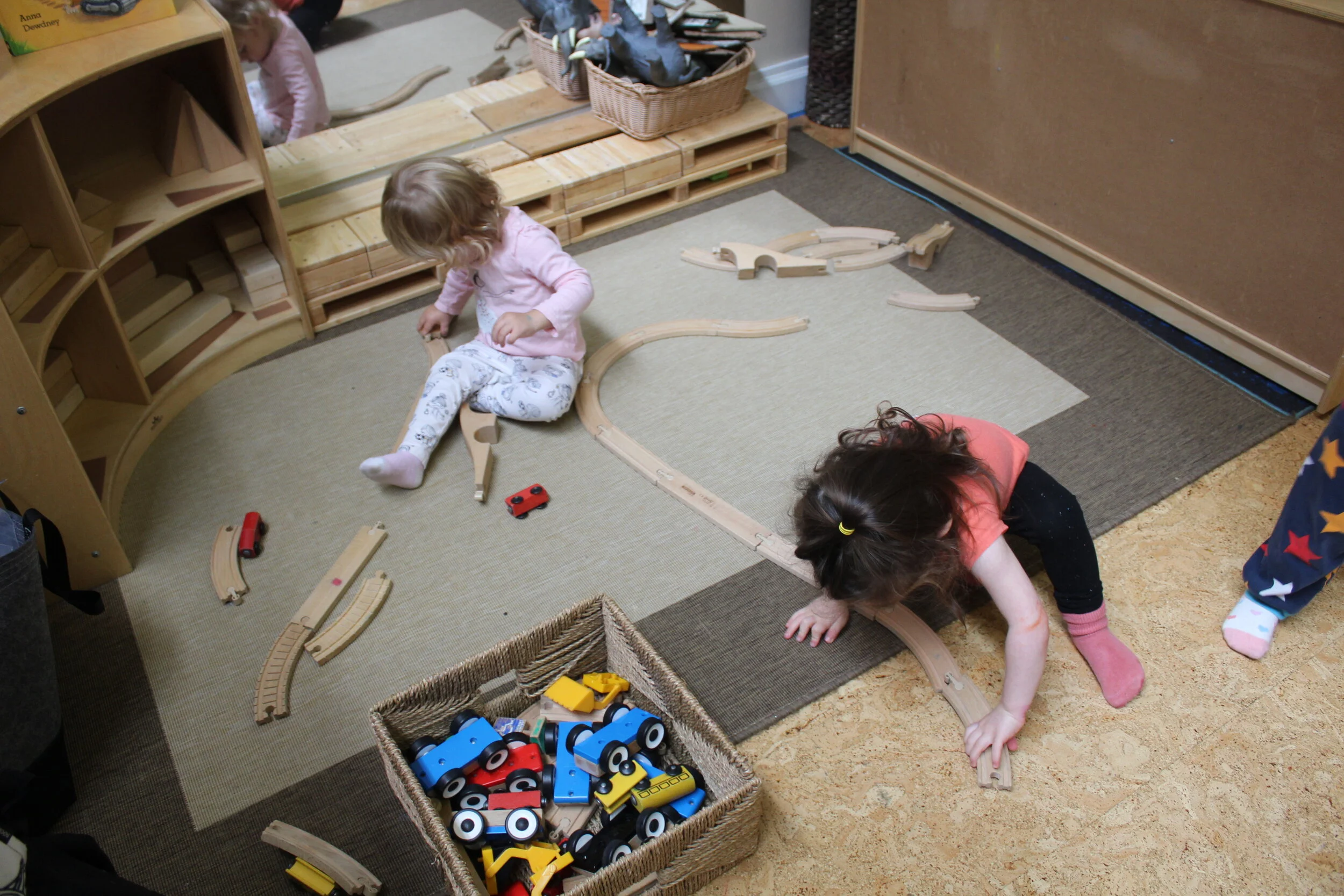  Annabelle took some train tracks from the basket and began building and connecting them. As children learn to interact with the train set, they learn to maneuver them to make them fit. She focuses and concentrates as she interlocks both ends, making