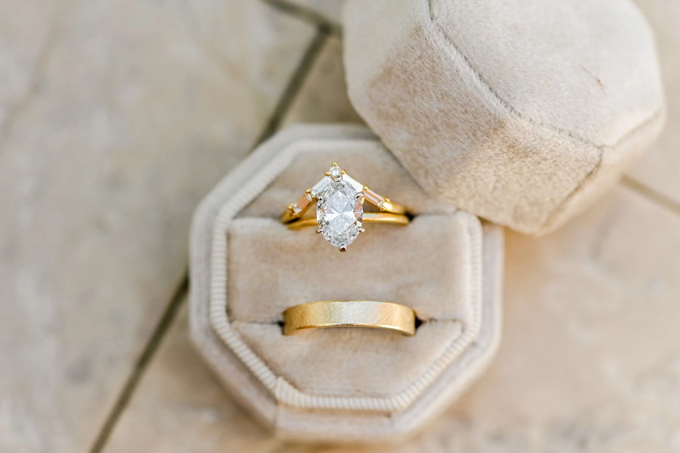 Close-up of a gold engagement ring with a large oval diamond in a beige jewelry box.