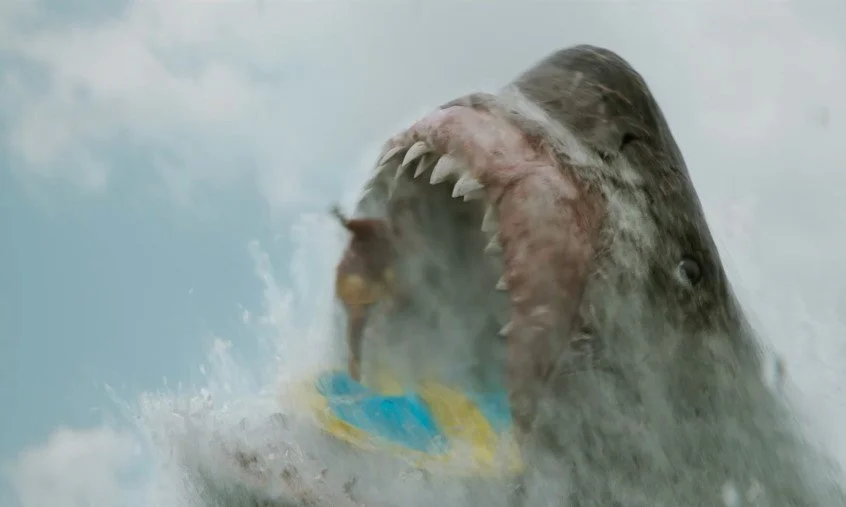 A large shark breaching the water's surface with its mouth open, showing sharp teeth, and spray around it.