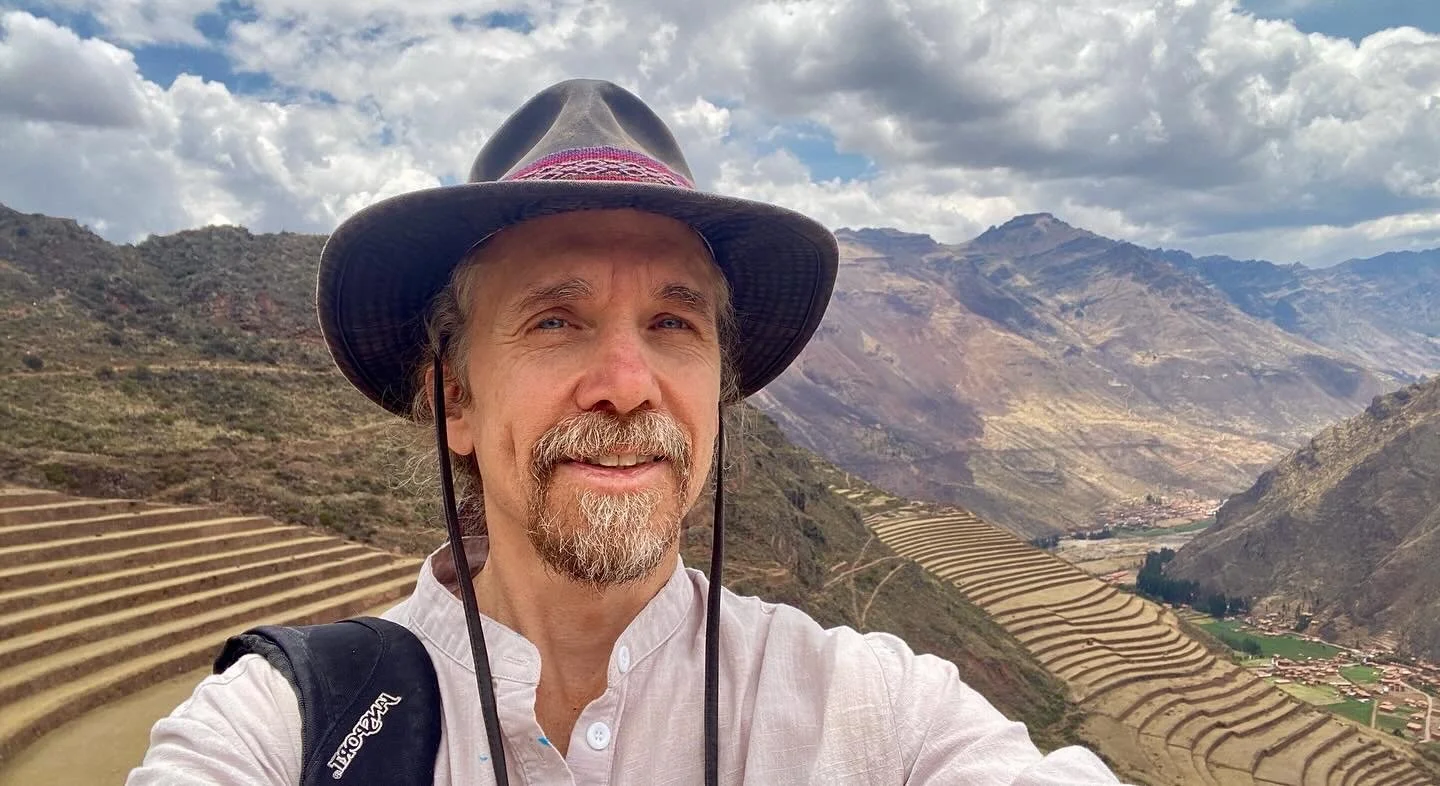 a man with a hat stands before a grand vista atop the ruins in Pisac, in the Sacred Valley of Peru.