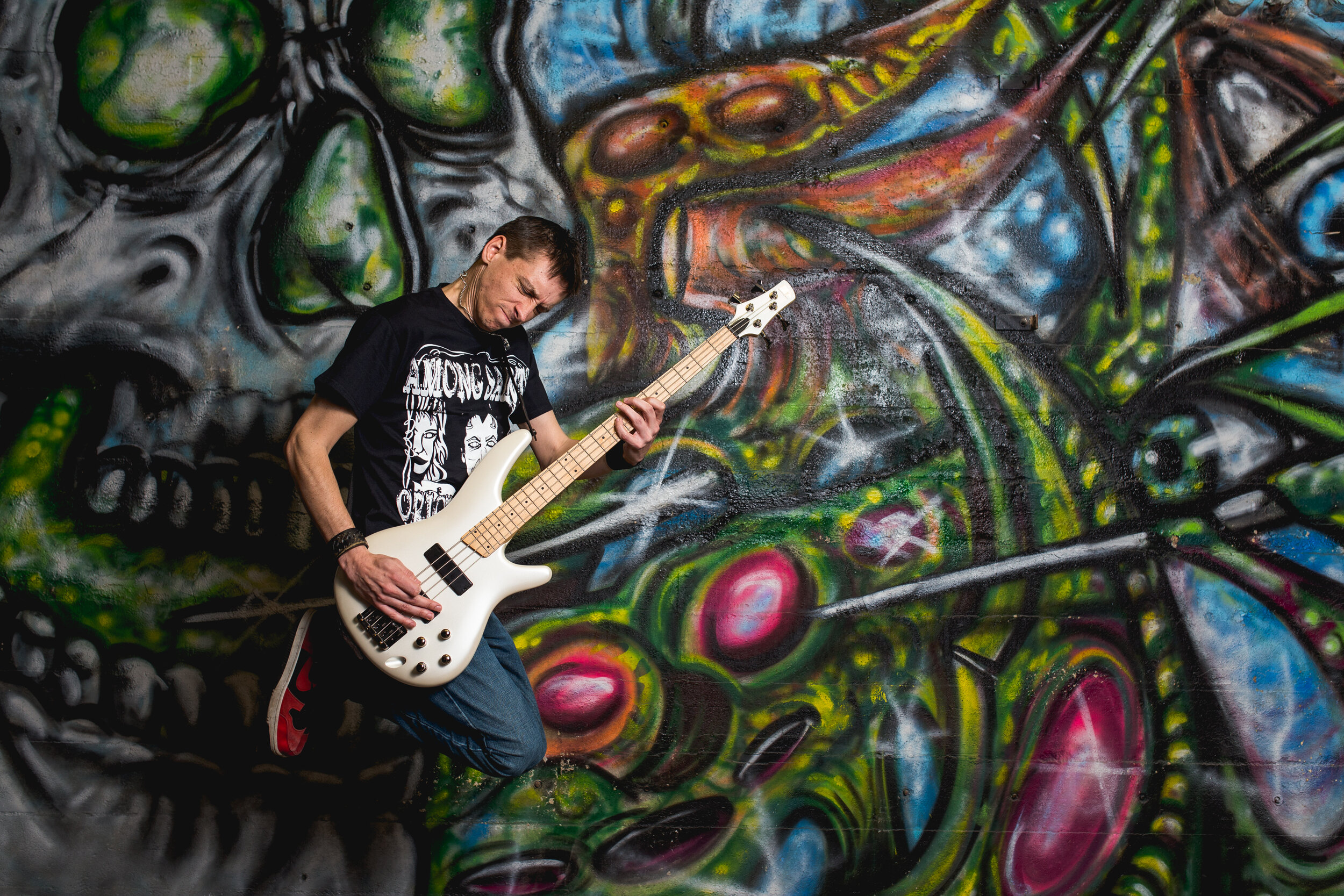 Photo of senior jumping in the air with a guitar in front of graffiti 