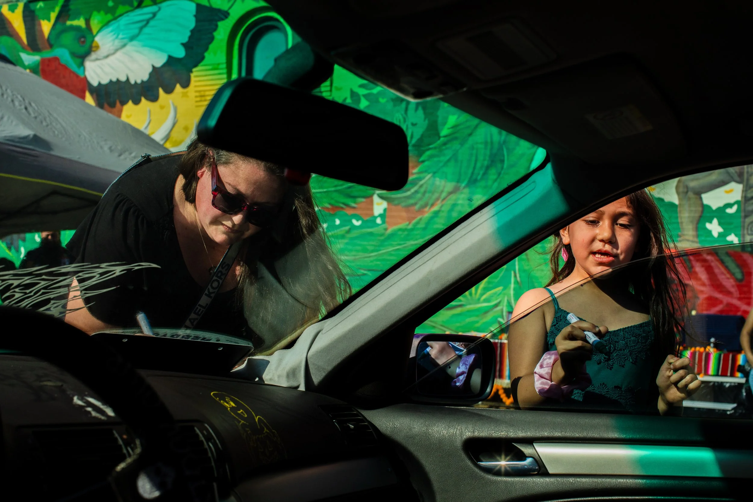  A woman and a girl use paint pens to write messages on a car for dia de los muertos. 