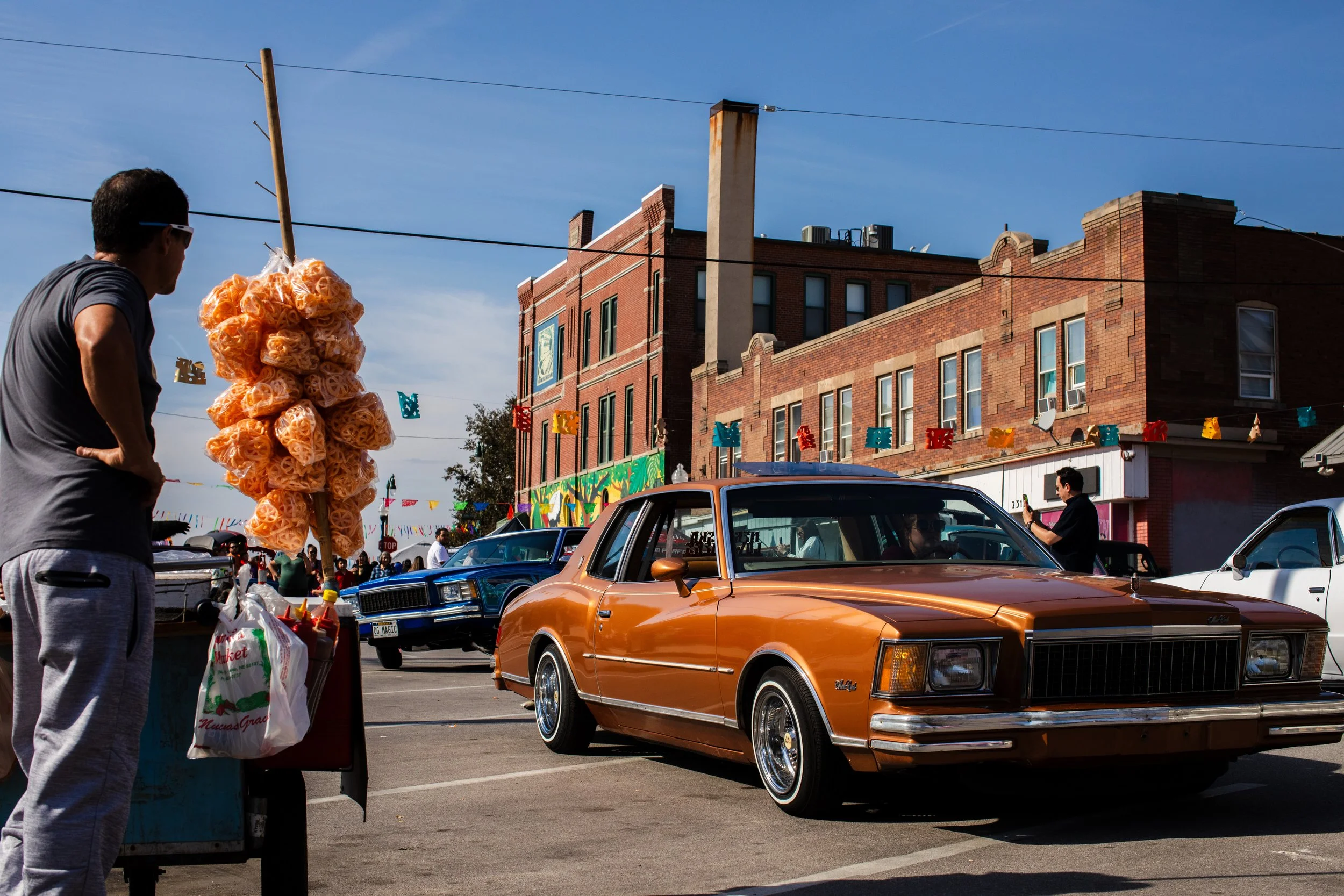  In Omaha, a vendor selling duritos watches the low riders leaving the car show to line up for the dia de los muertos parade later. 
