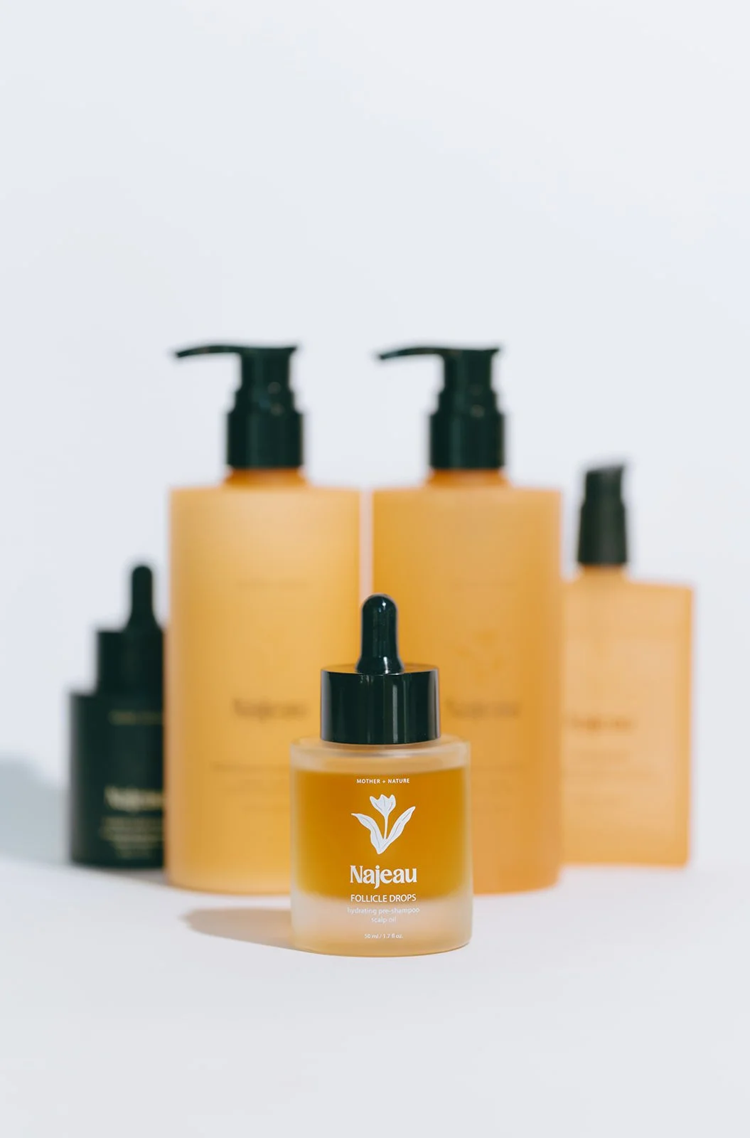 A small bottle of Najeau Follicle Drops with a dropper cap in front of larger bottles with pump dispensers, all on a white background.