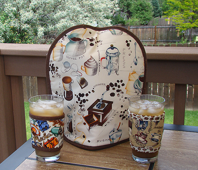 Architecture of Coffee French press cover over pitcher of iced coffee, with two Kup Kollars to keep coffee cold in the glass. Design is different on either side of all Koffee Kozees .