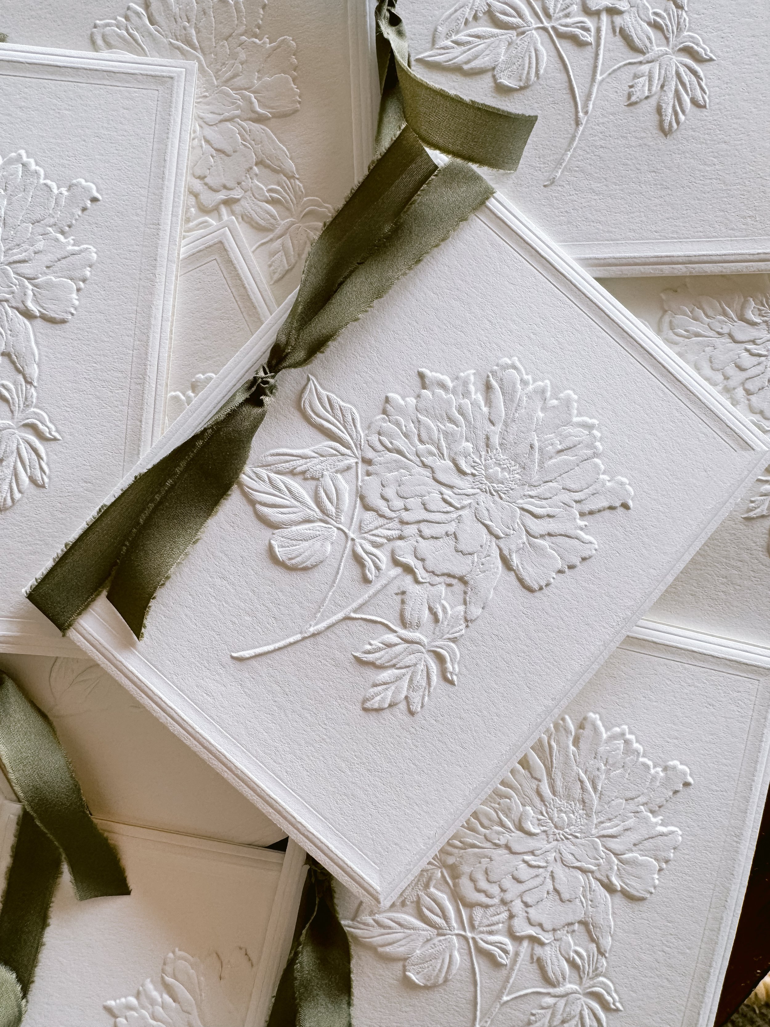 White embossed floral greeting card with a black satin ribbon tied around it.
