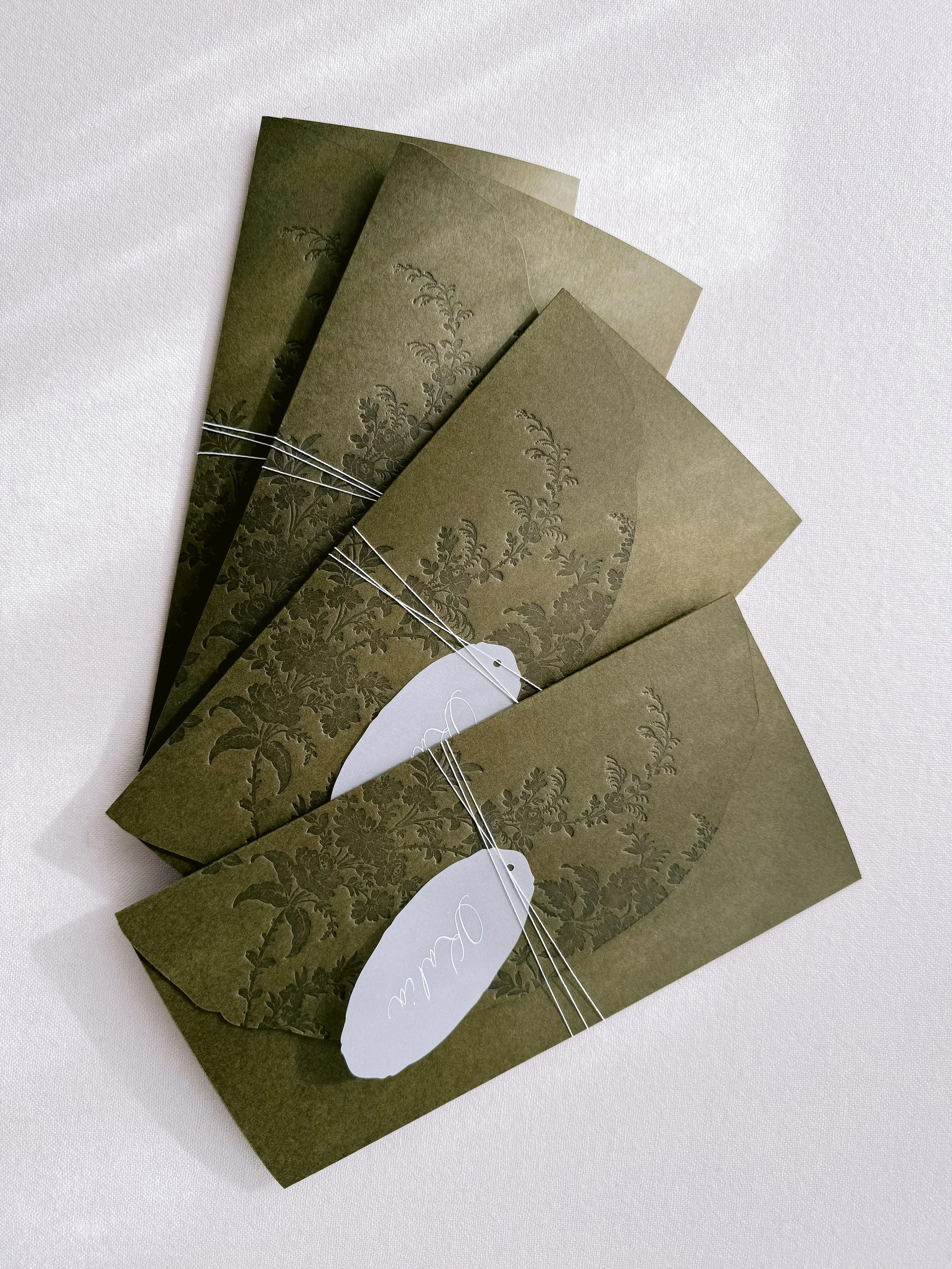 Group of olive green paper envelopes with floral patterns, tied together with white string, and a white oval tag with a handwritten message.