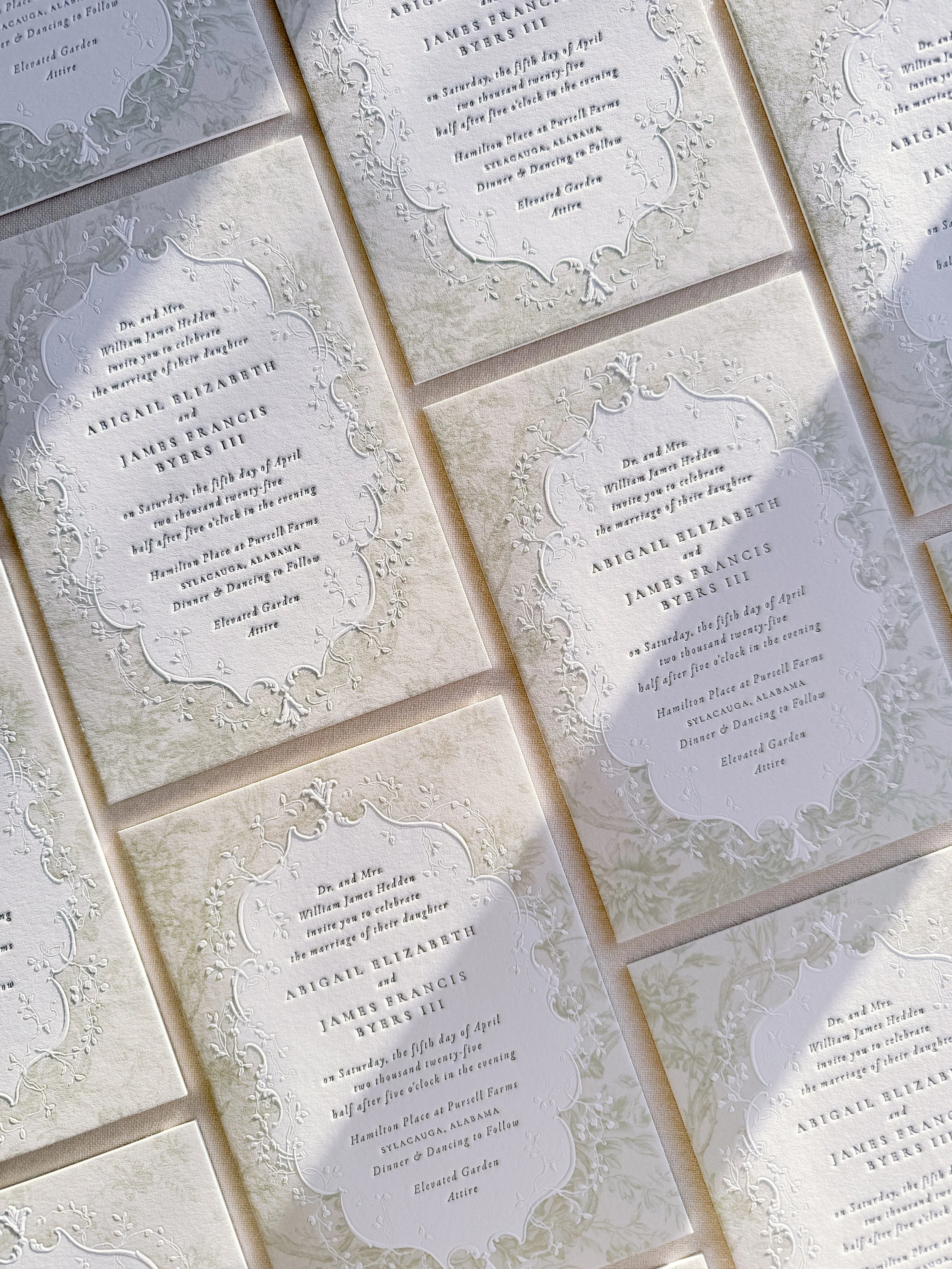 Wedding invitations with ornate embossed floral border design in white and cream tones.