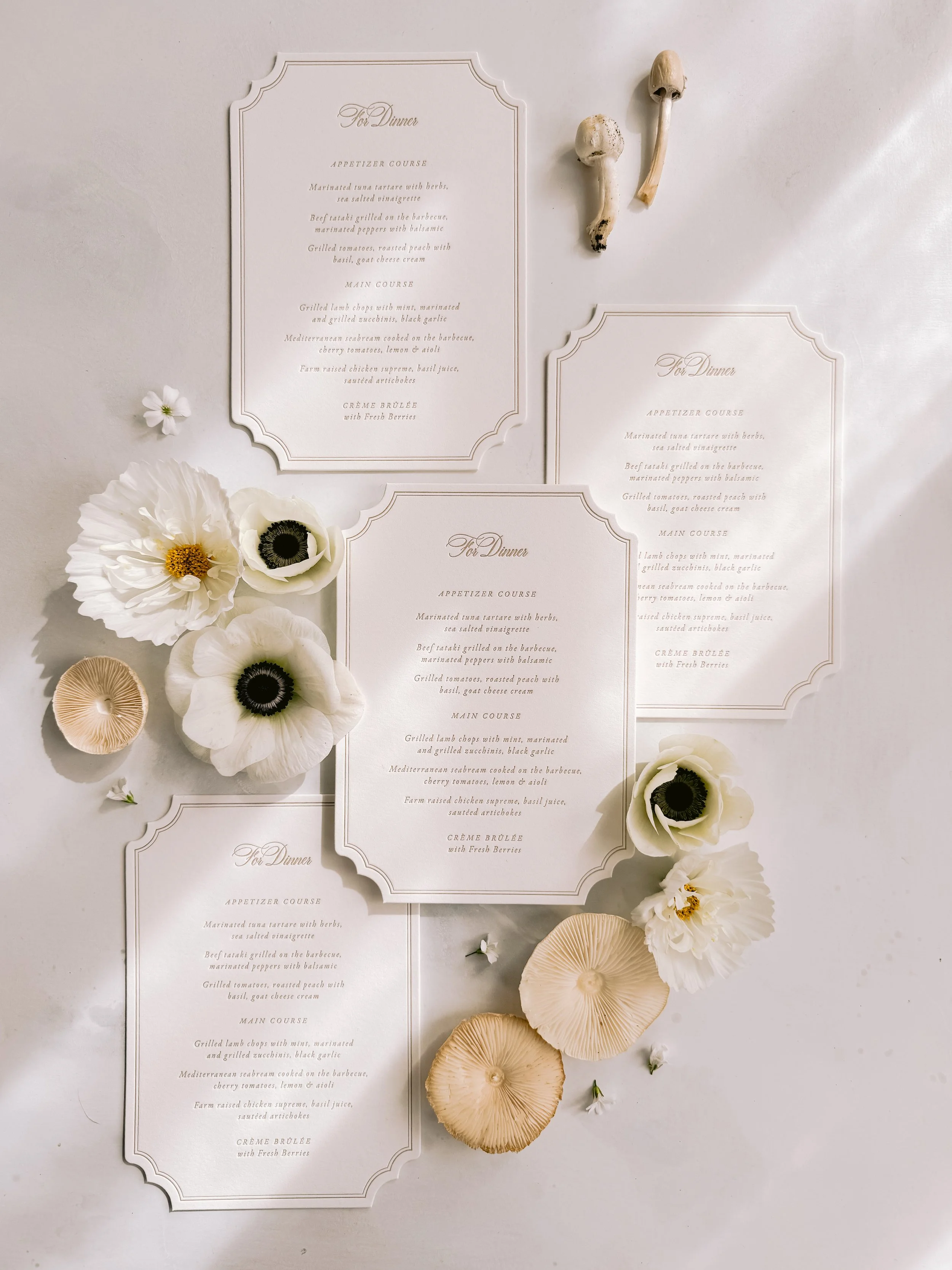 Set of four elegant dinner menus surrounded by white flowers, mushrooms, and small white blossoms on a white background.