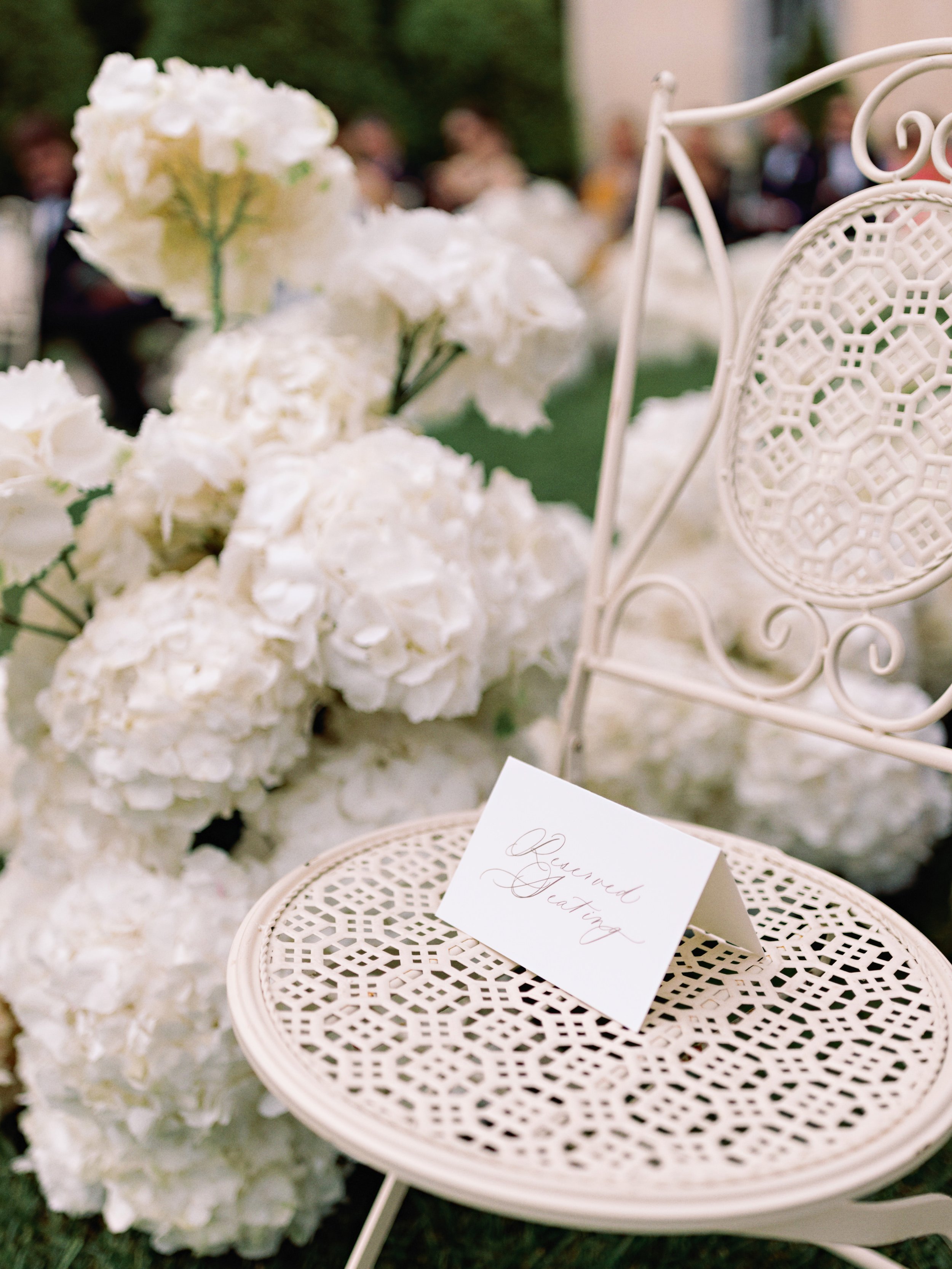 Wedding reception decor with white hydrangeas, a white ornate metal chair, and a 'Reserved Seating' card