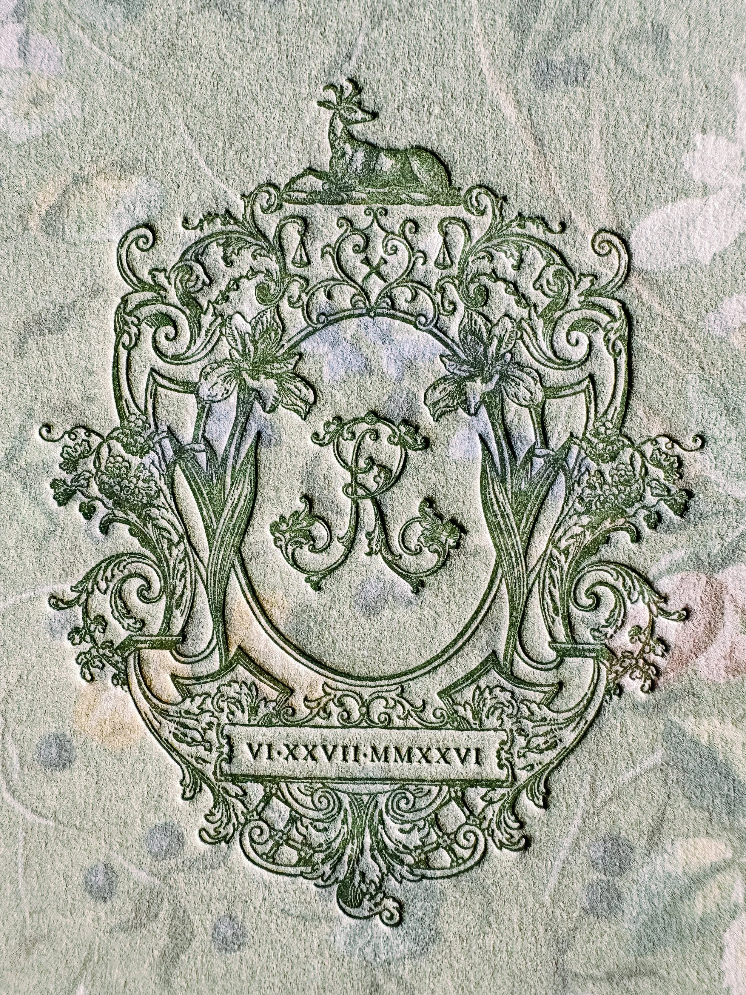 Close-up of an ornate, vintage crest or heraldic emblem with floral and animal motifs, engraved on paper, with a date inscription in Roman numerals.