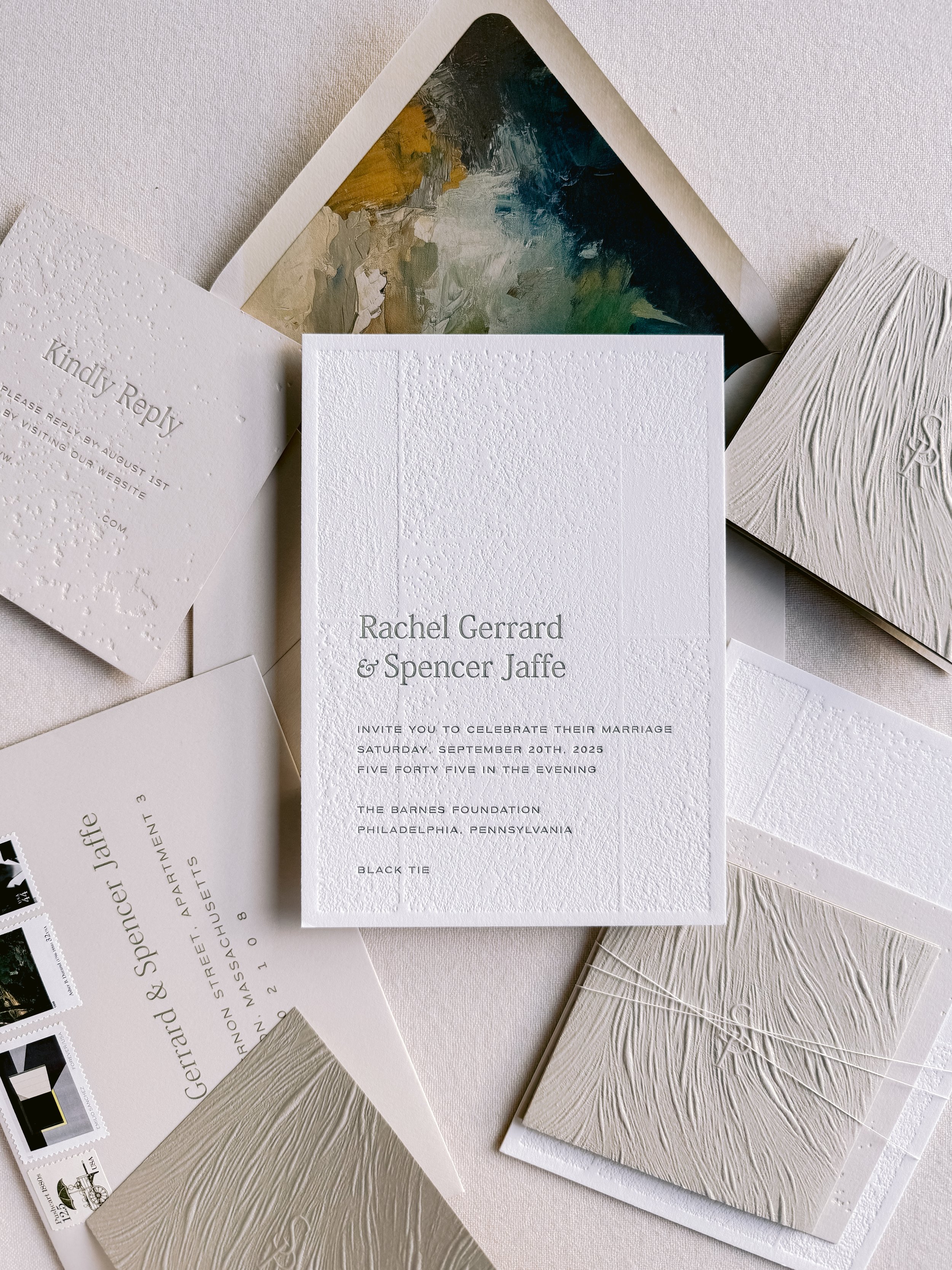 Wedding invitation suite featuring textured white paper with embossed details, surrounding abstract paintings and decorative cards.