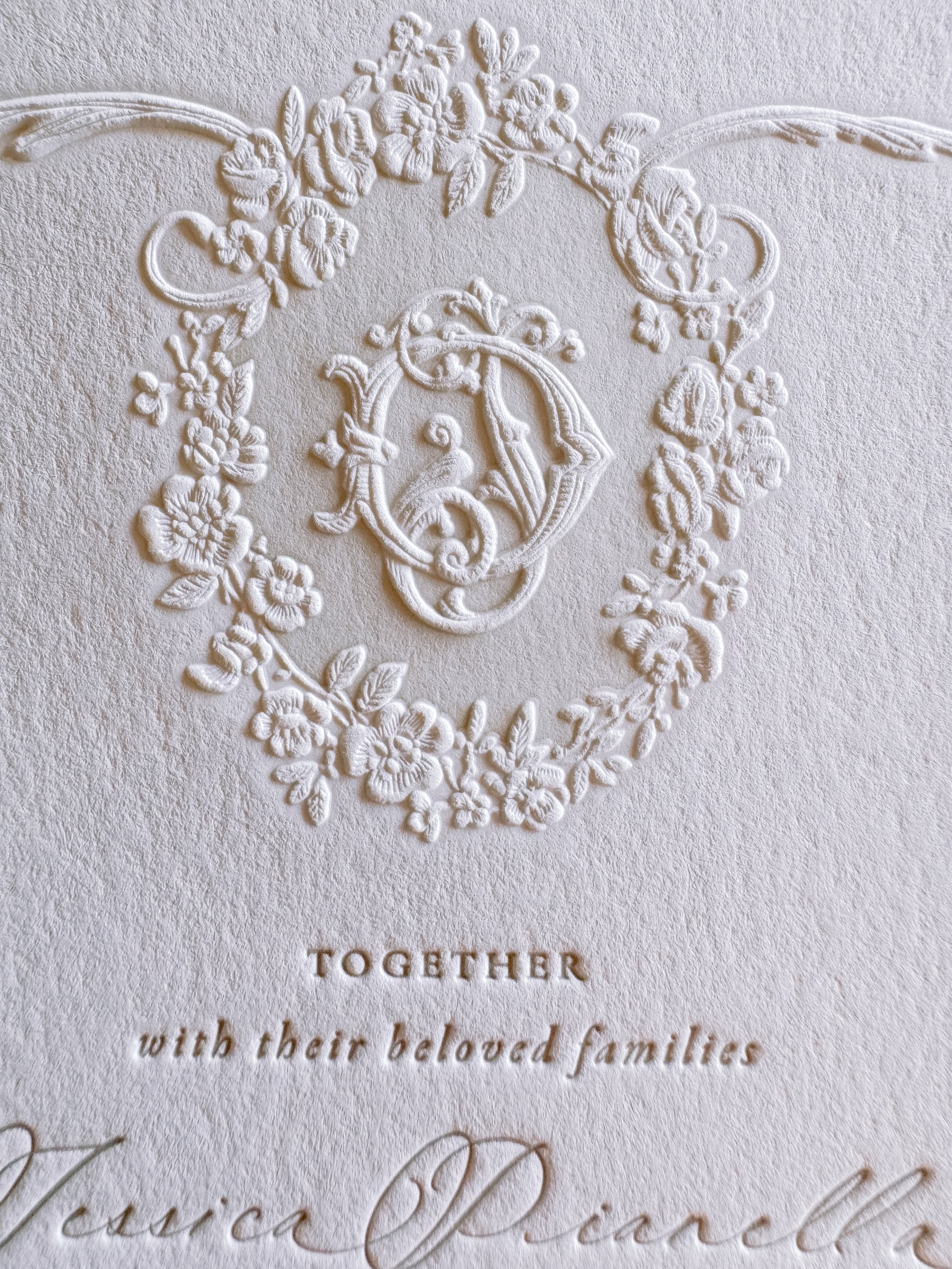 Close-up of a wedding invitation with embossed floral design and elegant script text reading 'TOGETHER with their beloved families'.