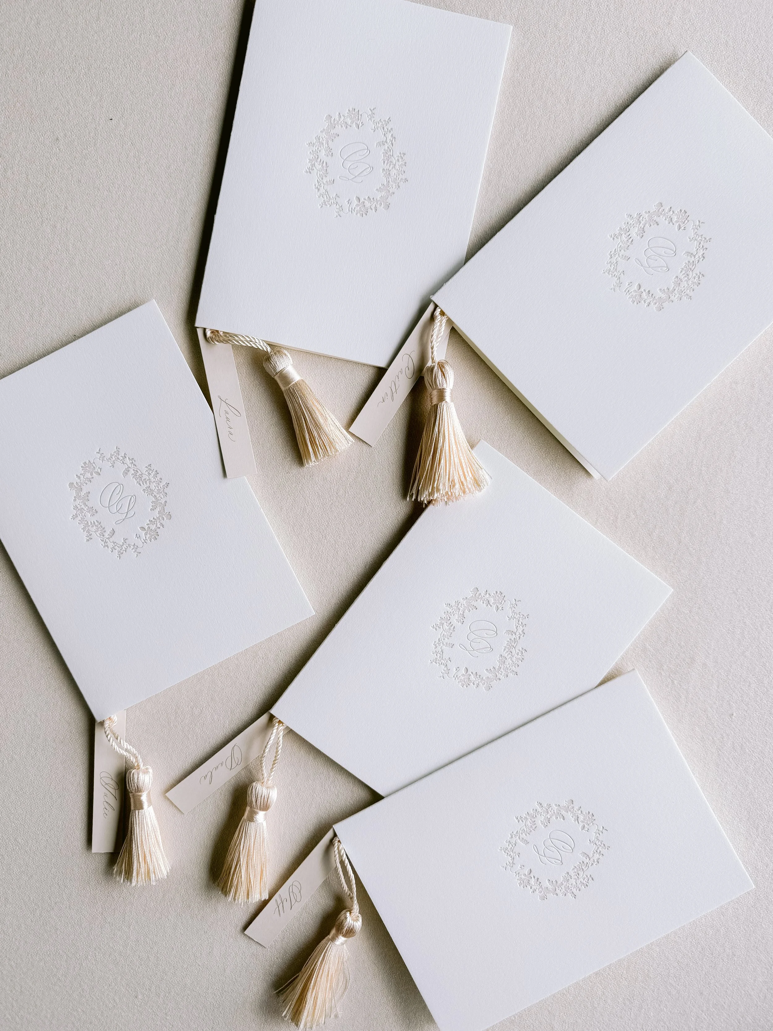 Several white cards with decorative borders and tassels, likely wedding or event invitations, arranged on a light surface.