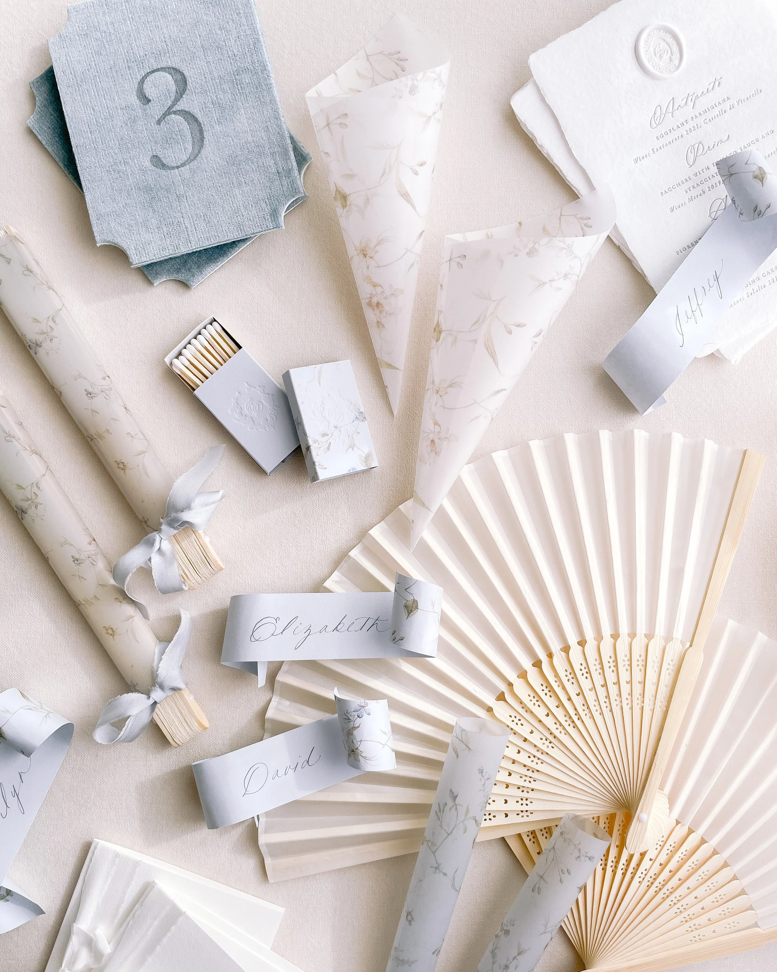Decorative paper cones, fans, and name tags on a light-colored surface, likely for a wedding or celebration.