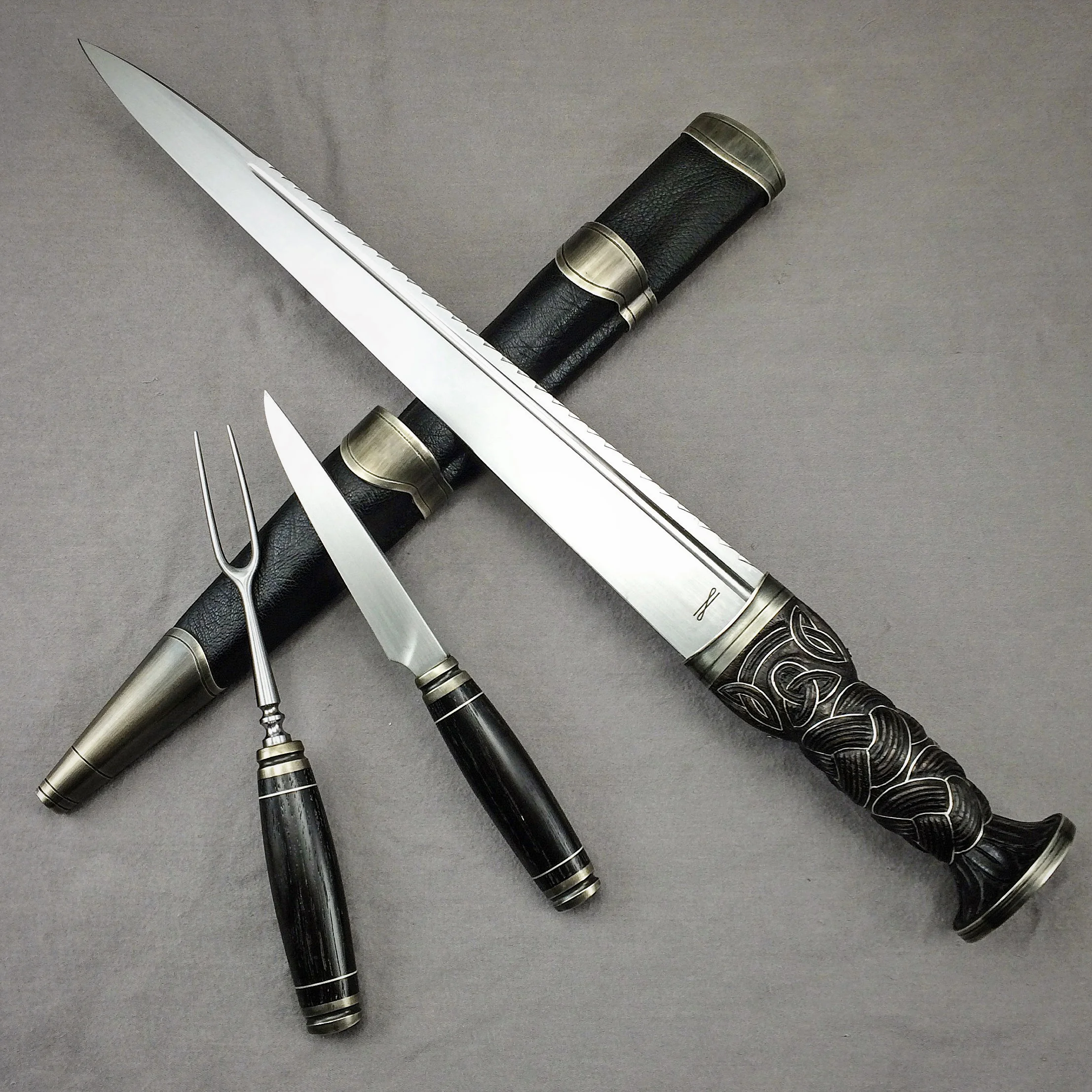 Scottish Dirk with sheath, by-knife and fork. Blades are forged 5160 spring steel, the Dirk handle is carved and inlayed walnut, the knife and fork handles are Bog Oak. Inlays are fine silver, fittings are antiqued nickel-silver, sheath is leather-wrapped wood.