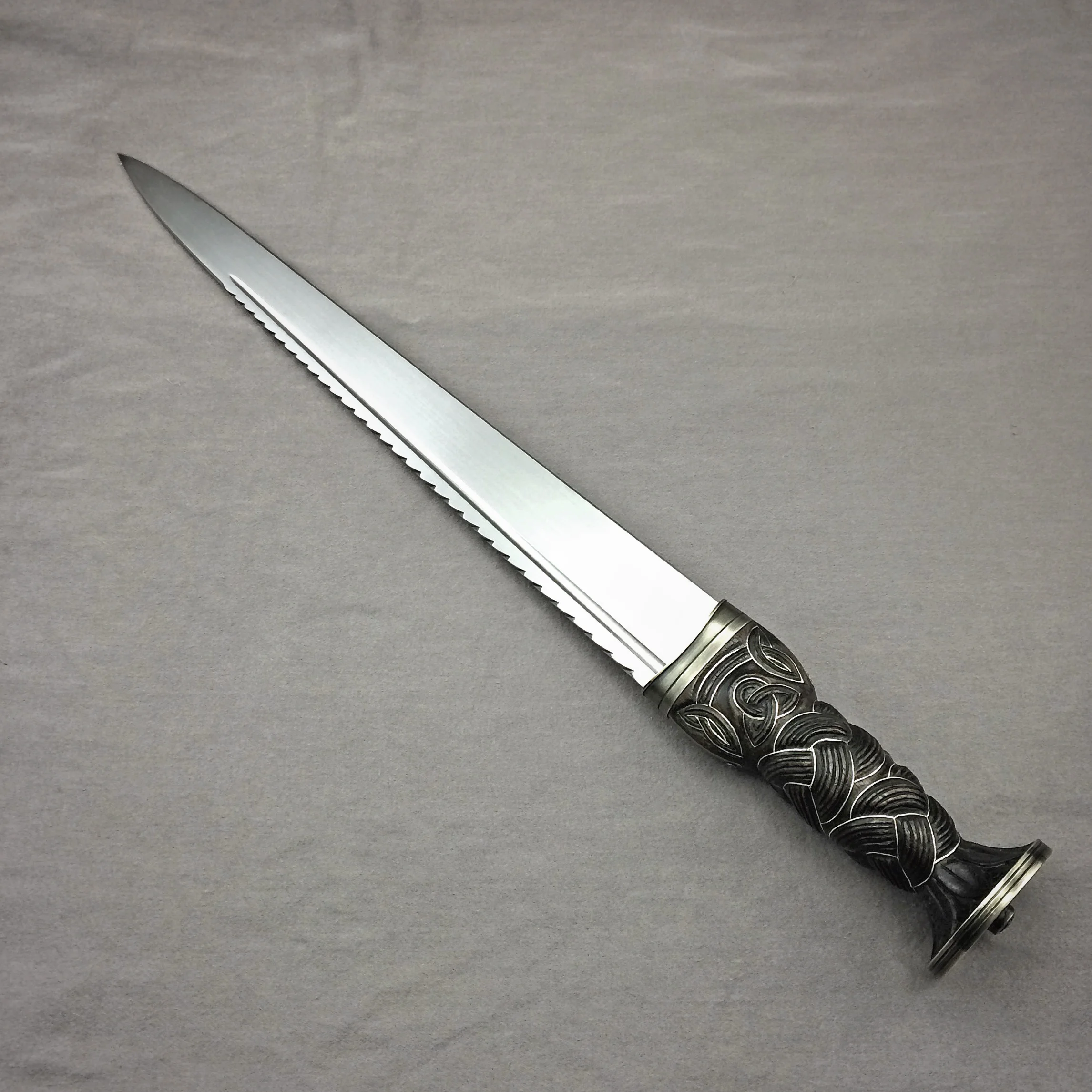 Scottish Dirk, 12" 5160 blade with filework, fuller, and slight false edge at tip. Handle is walnut, carved and dyed, inlayed with fine silver,with antiqued and engraved nickel-silver ferrule and pommel cap.