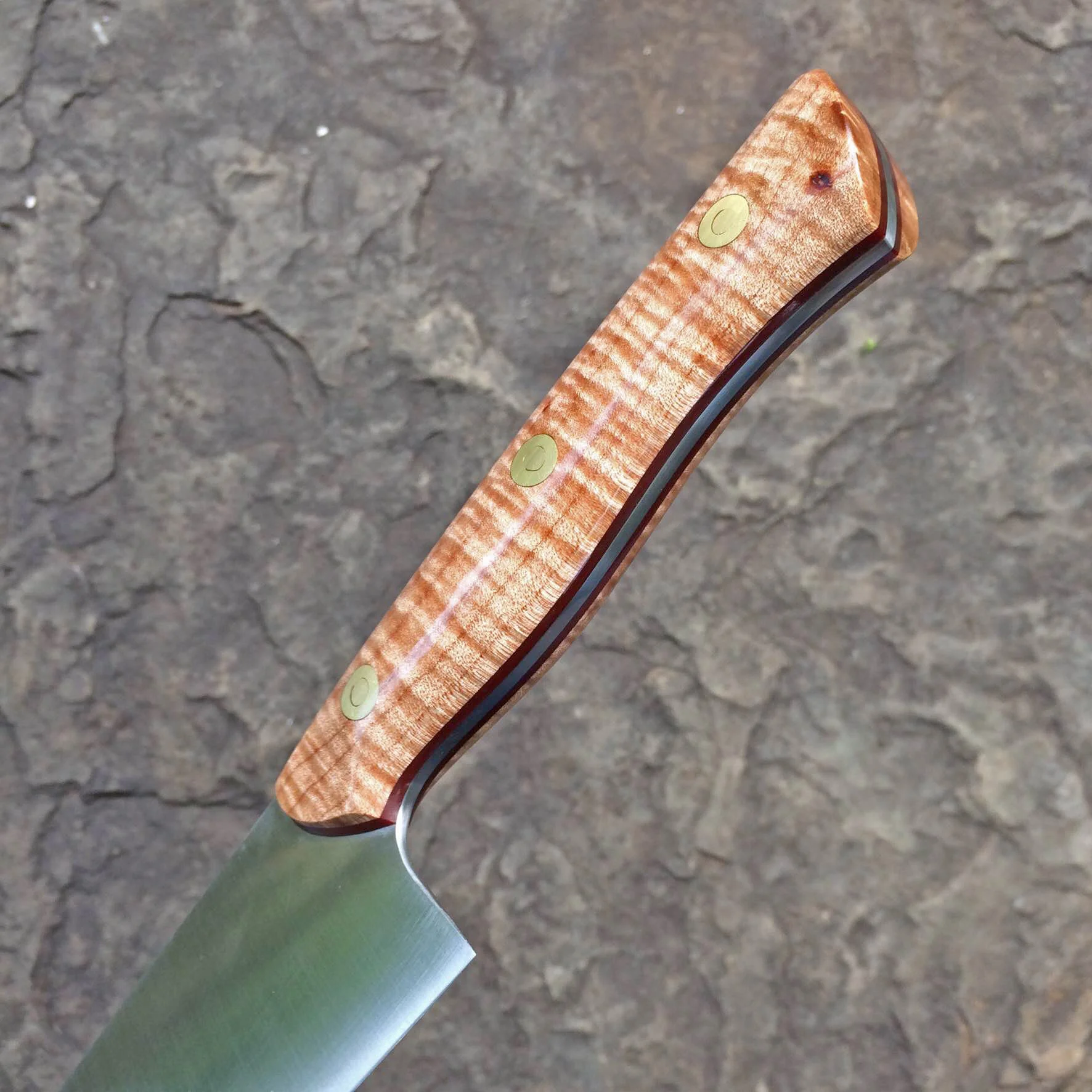 Detail of bolster-less handle, curly maple, and red liners.
