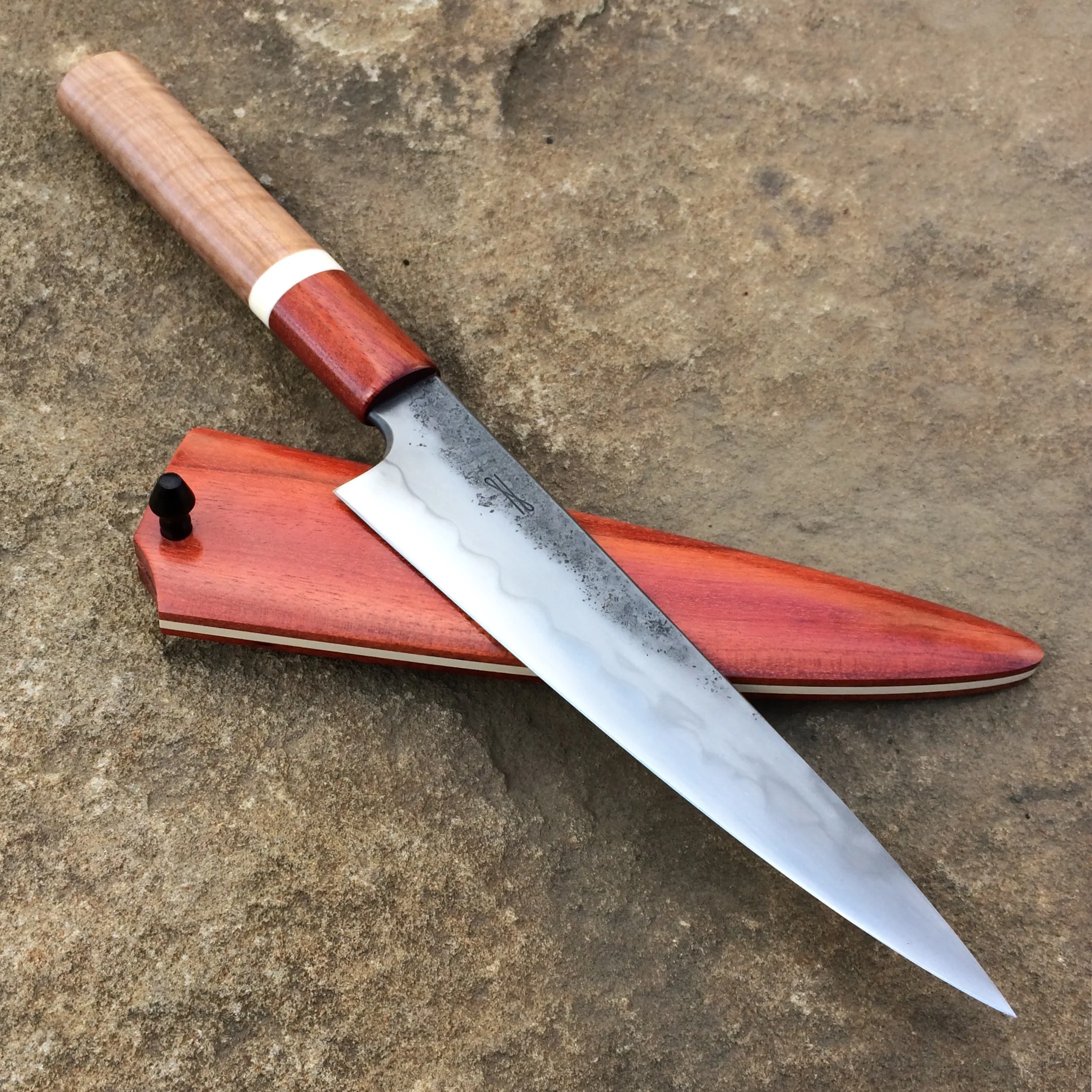 6.5" Line Knife. Forged W2 steel, differentially heat-treated. Oval handle is Musclewood, Bloodwood, and Bone. Saya is Bloodwood with an ivory paper Micarta spacer.