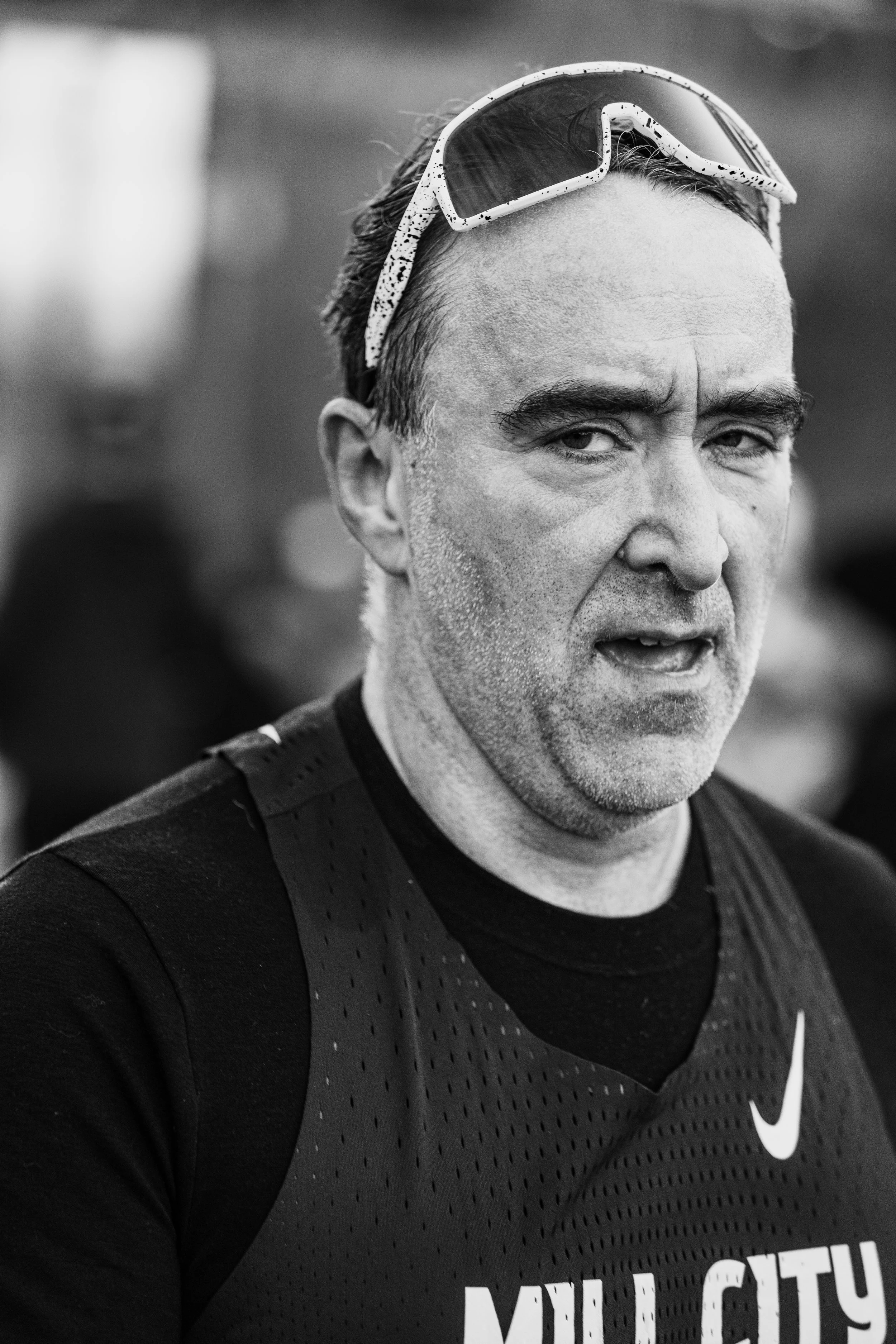 A man with soaked hair, wearing sunglasses on his head and a black sleeveless sports shirt with the Nike logo and the words "MILL CITY". He appears sweaty and tired.