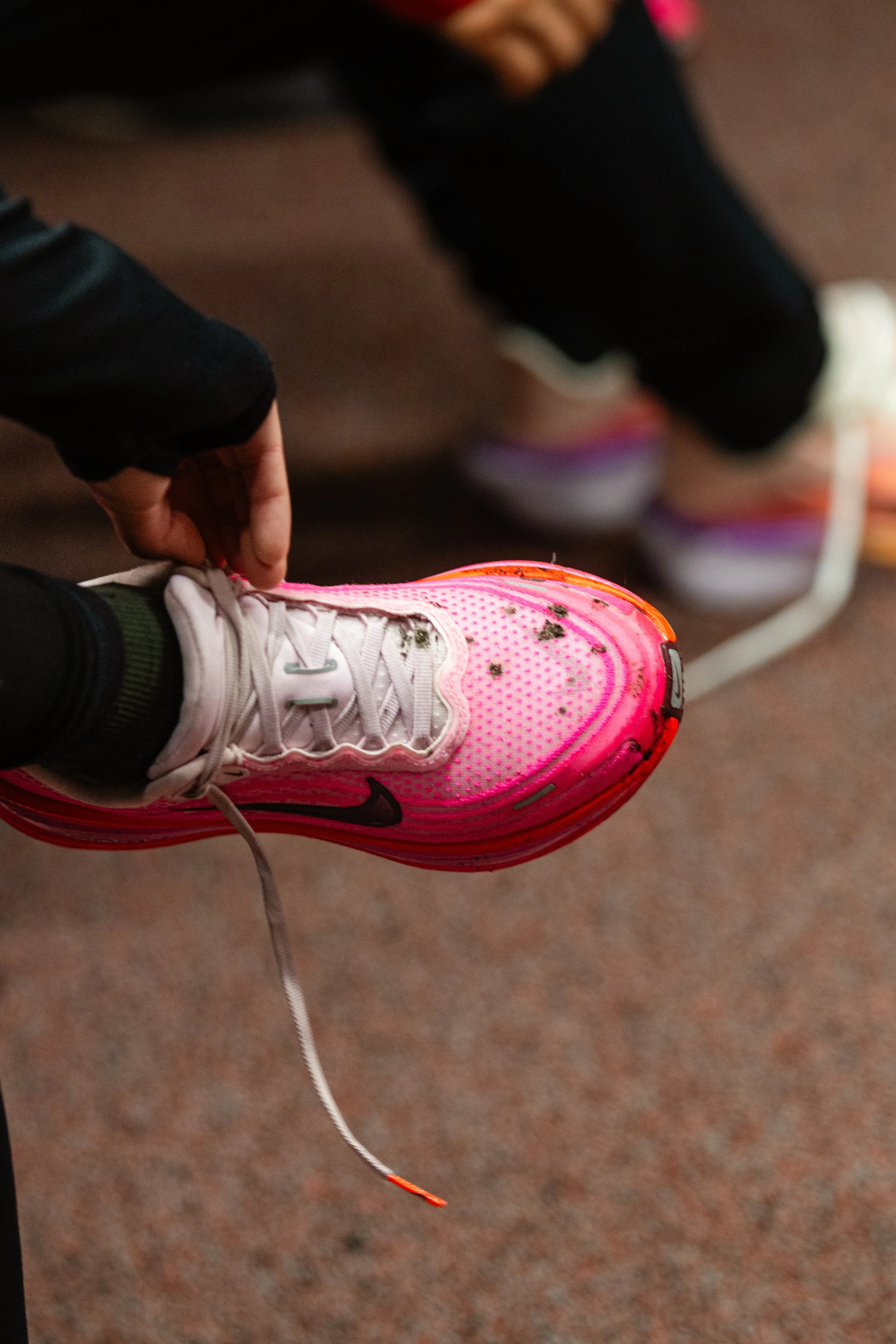 A person wearing pink and white athletic shoes and black leggings is tying the shoelaces of their sneaker.