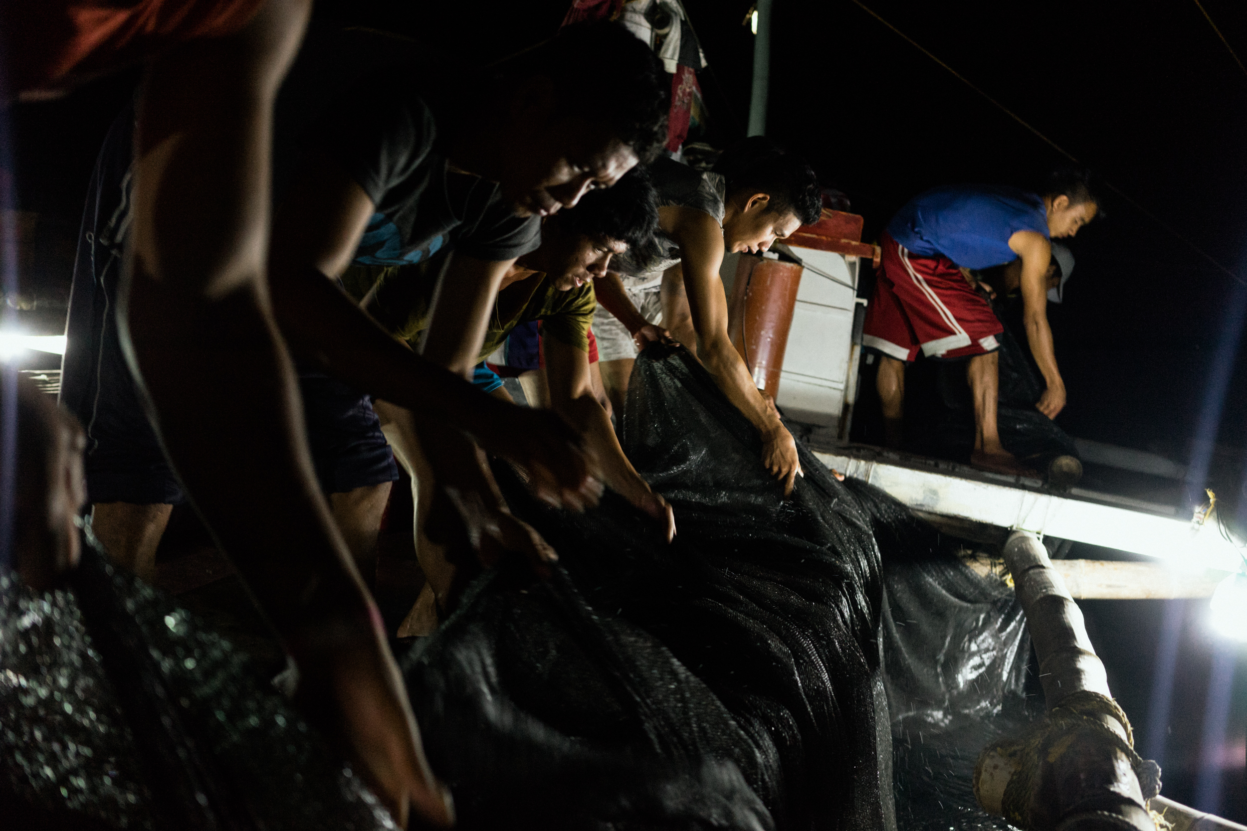  Kalibo, Philippines - September 21, 2015: The crew of a local fishing boat fish for their night's catch. Members of the crew, who make approximately 35 USD per month, have expressed their desire to work on a larger fishing vessel for the promise of 