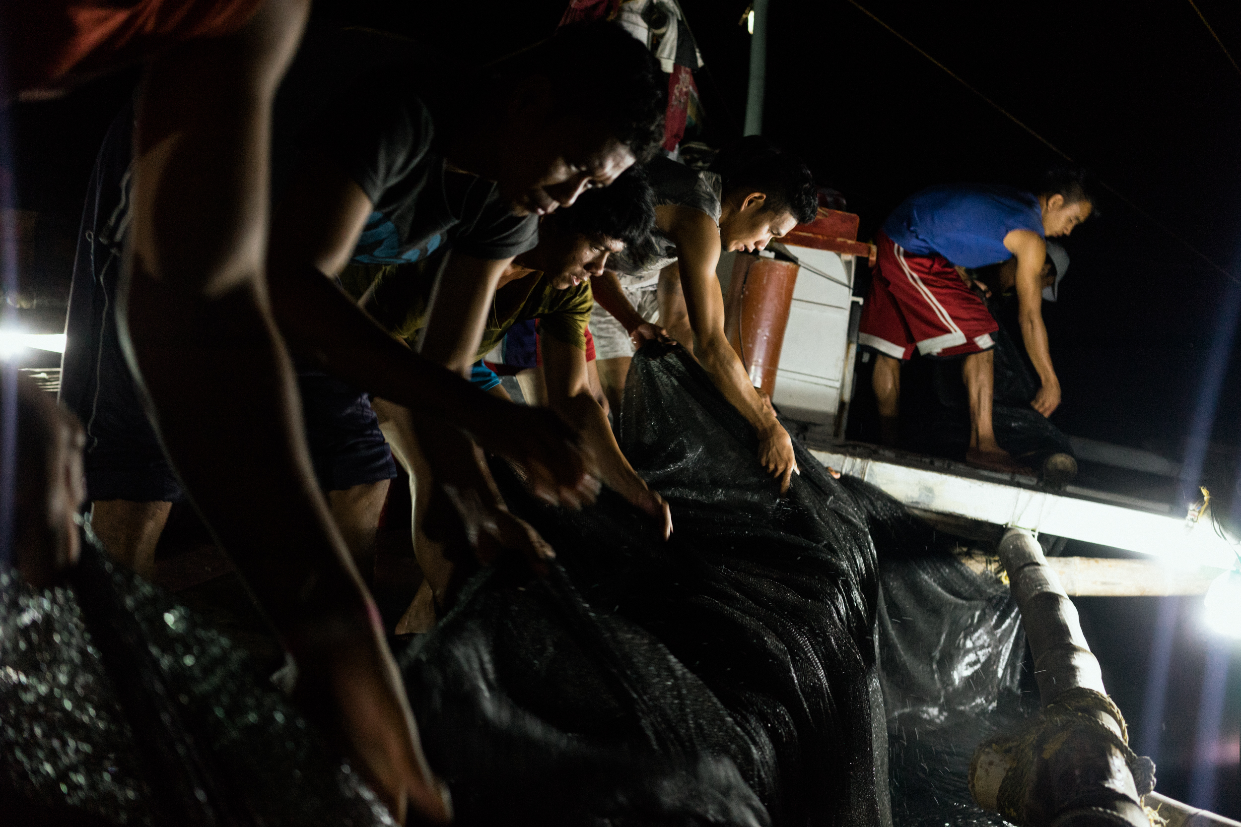 Kalibo, Philippines - September 21, 2015: The crew of a local fishing boat fish for their night's catch. Members of the crew, who make approximately 35 USD per month, have expressed their desire to work on a larger fishing vessel for the promise of a higher income despite stories of fellow crewmembers about the forms of abuse that happen on such vessels. Hannah Reyes