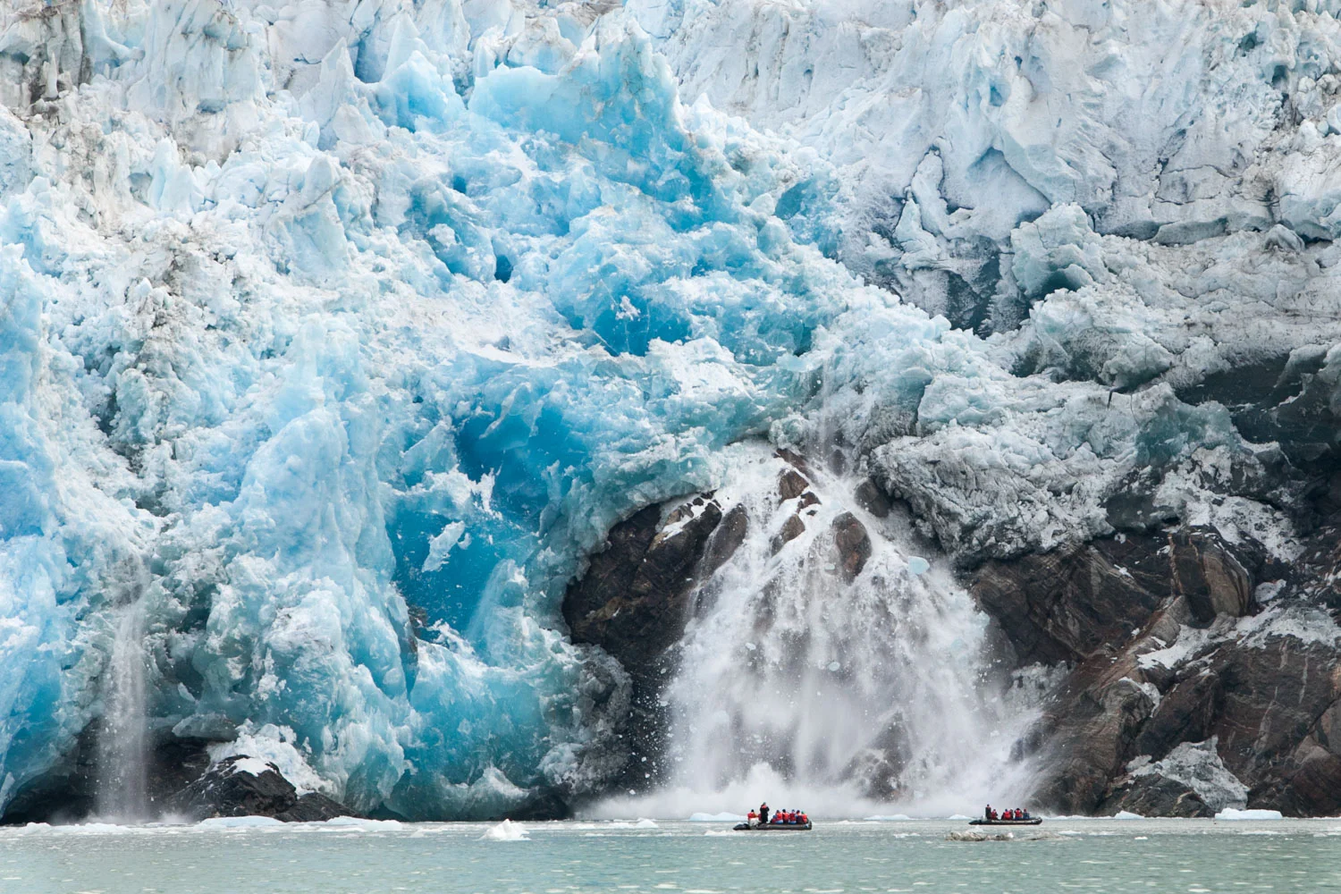 At the mouth of a glacier within Alaska's Inside Passage, travelers in Zodiac boats navigate water around icebergs and witness calving.