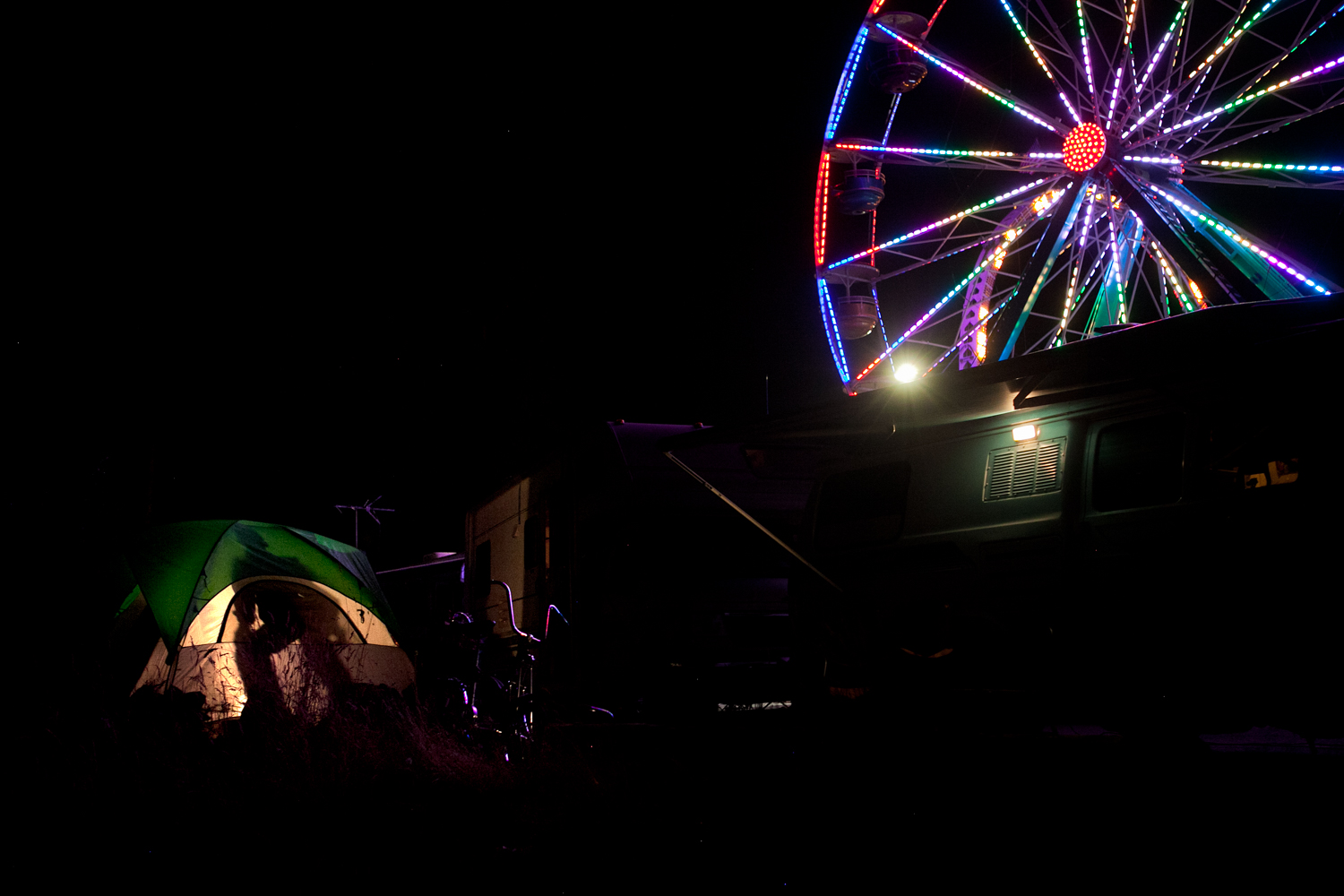  Workers setup camp and live in close proximity to the carnival grounds. At night, a man prepares for bed in his tent while the Ferris Wheel illuminates the surrounding area. 