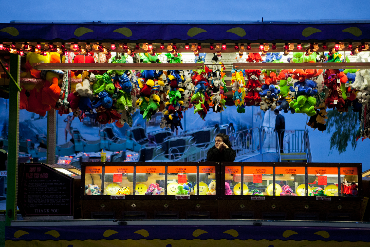  At each carnival location, workers are usually assigned to a specific ride, food stall, or game for the week’s duration. As night falls, a carnival worker waits for visitors to play her game. When the carnival is open, workers usually attend to ride
