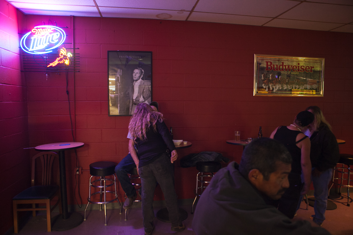 Five carnival workers (one man in the foreground, two couples in the background) spend some free time in a local bar. As the man sits at the bar, the two couples each engage in a kiss.
