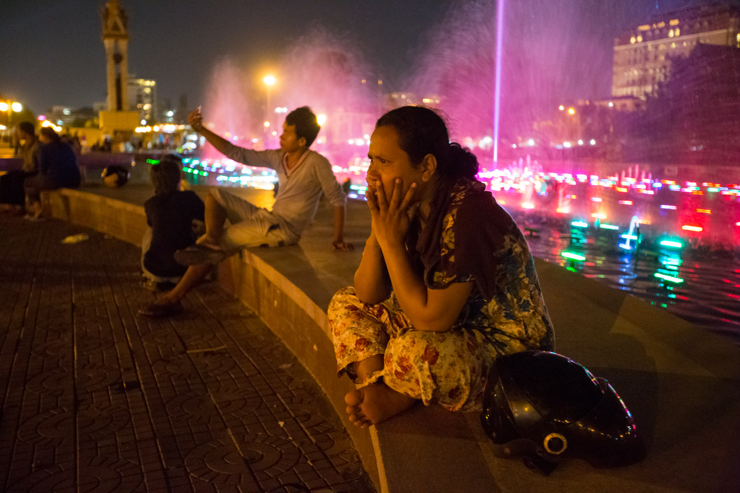In Phnom Pehn, Cambodia, a local sits near a night-time fountain light show.