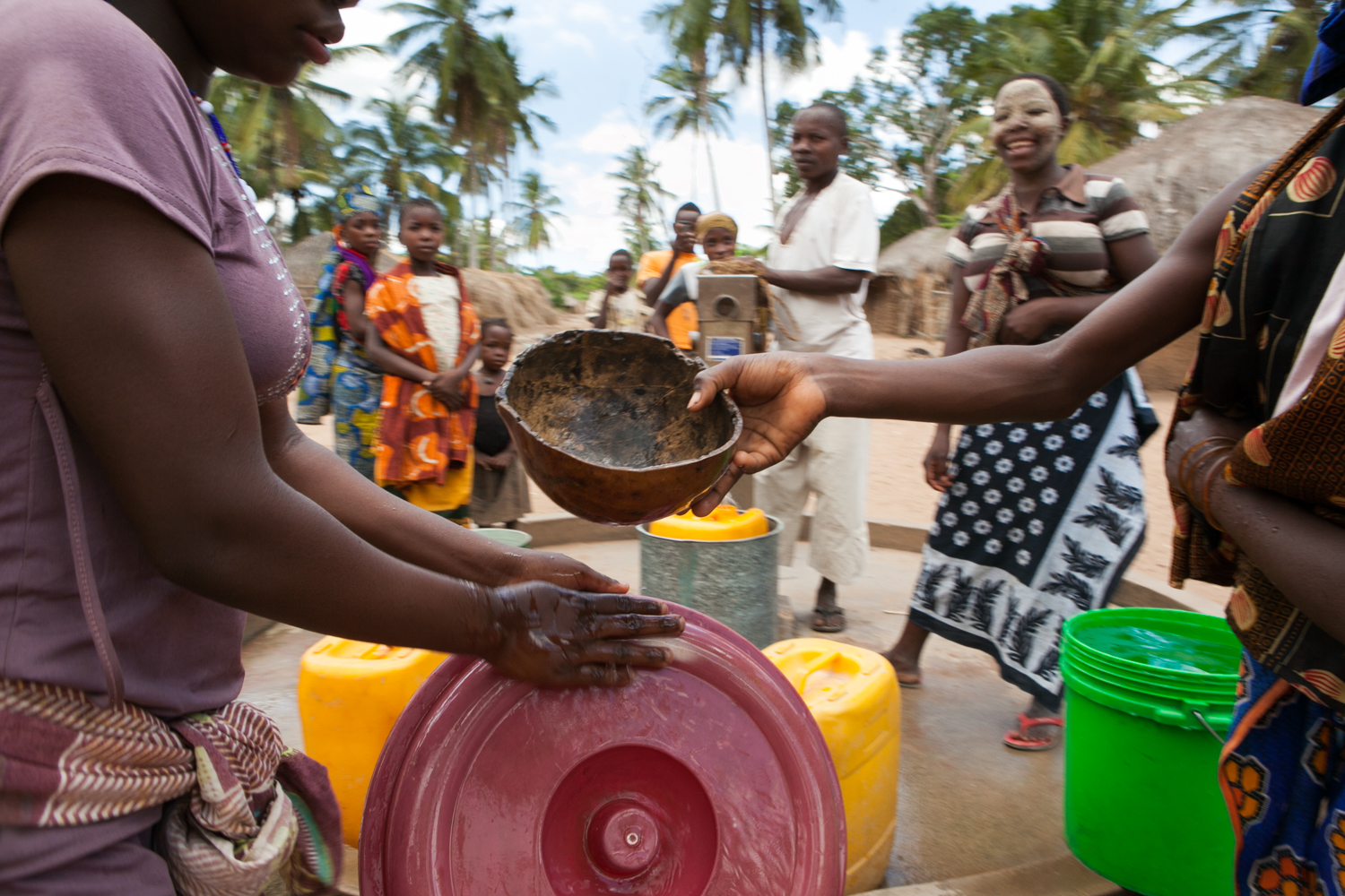  After pump repairs are complete, residents bring their colorful buckets and collect water. They oftentimes utilize a coconut shell for distributing water between buckets and washing their hands. 